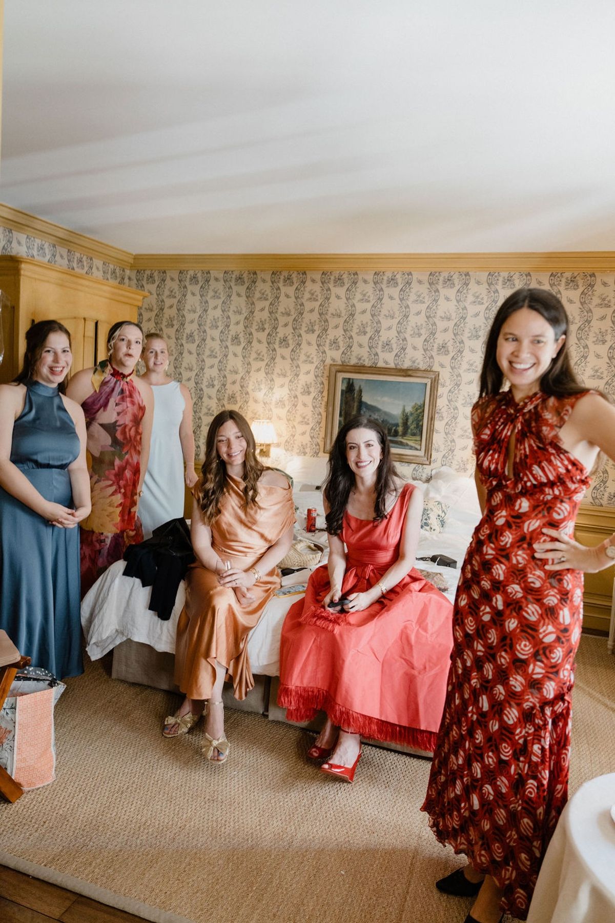 Bridesmaids in colourful jewel-tone gowns gathered around bed in chateau bedroom