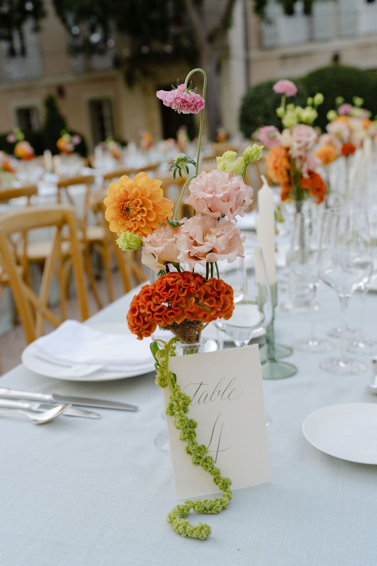 Centrepiece of orange dahlia coxcomb blush lisianthus and pink scabiosa with table number
