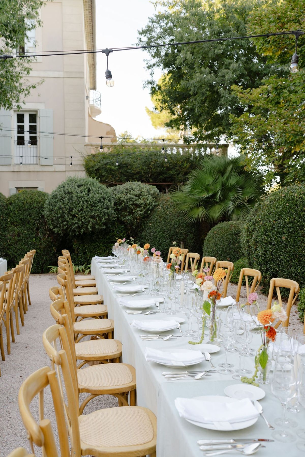 Long farm table in chateau garden with sage linen bistro chairs and string lights