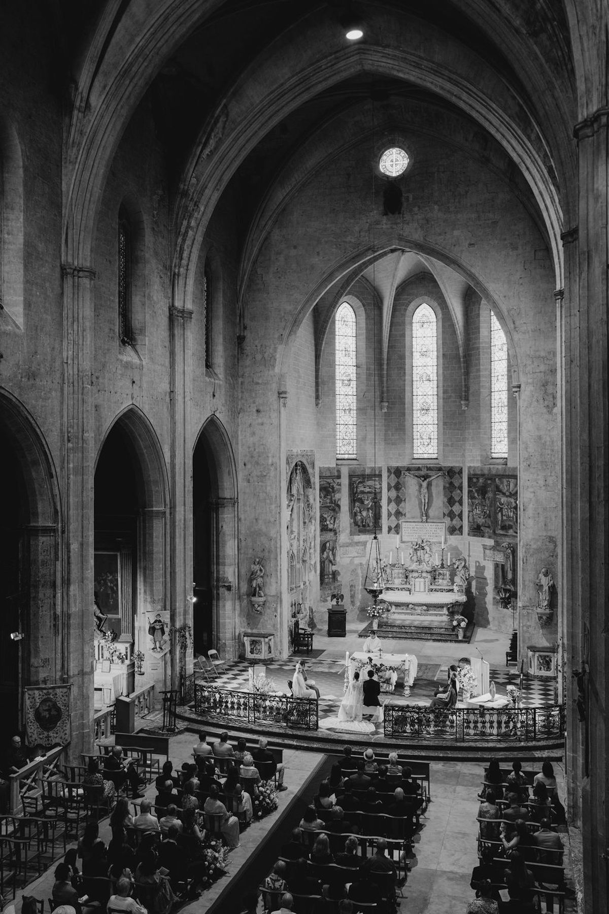 Black and white wide shot of couple at altar with gothic arches and rose window