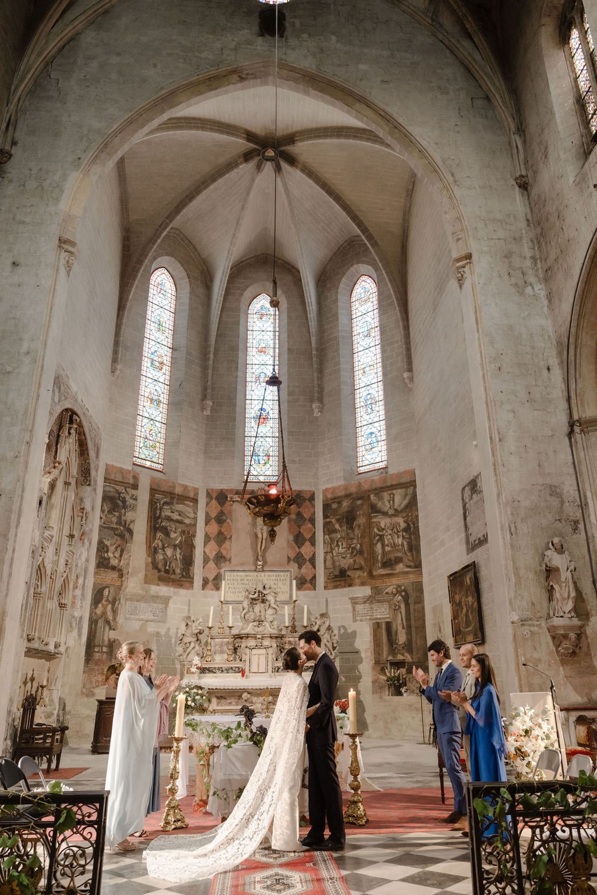 Bride and groom at altar with witnesses applauding around candle and floral altar