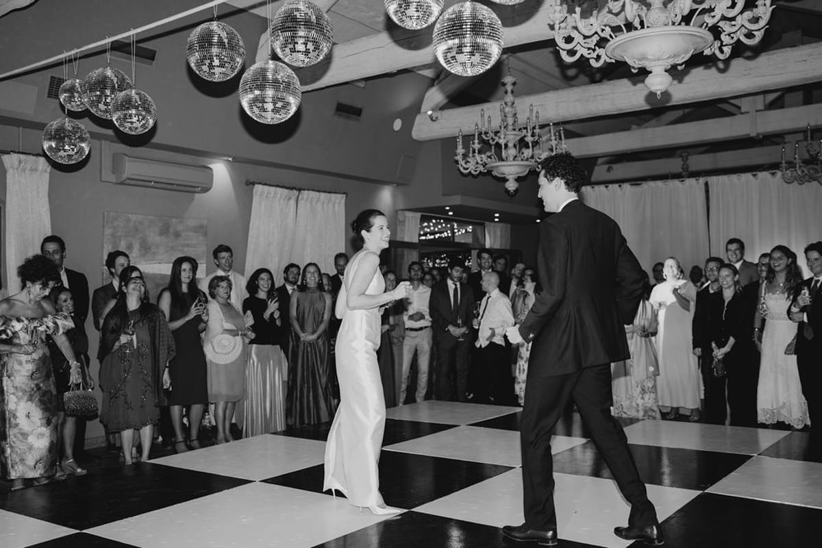 Couple first dance on checkered floor with guests around under disco balls