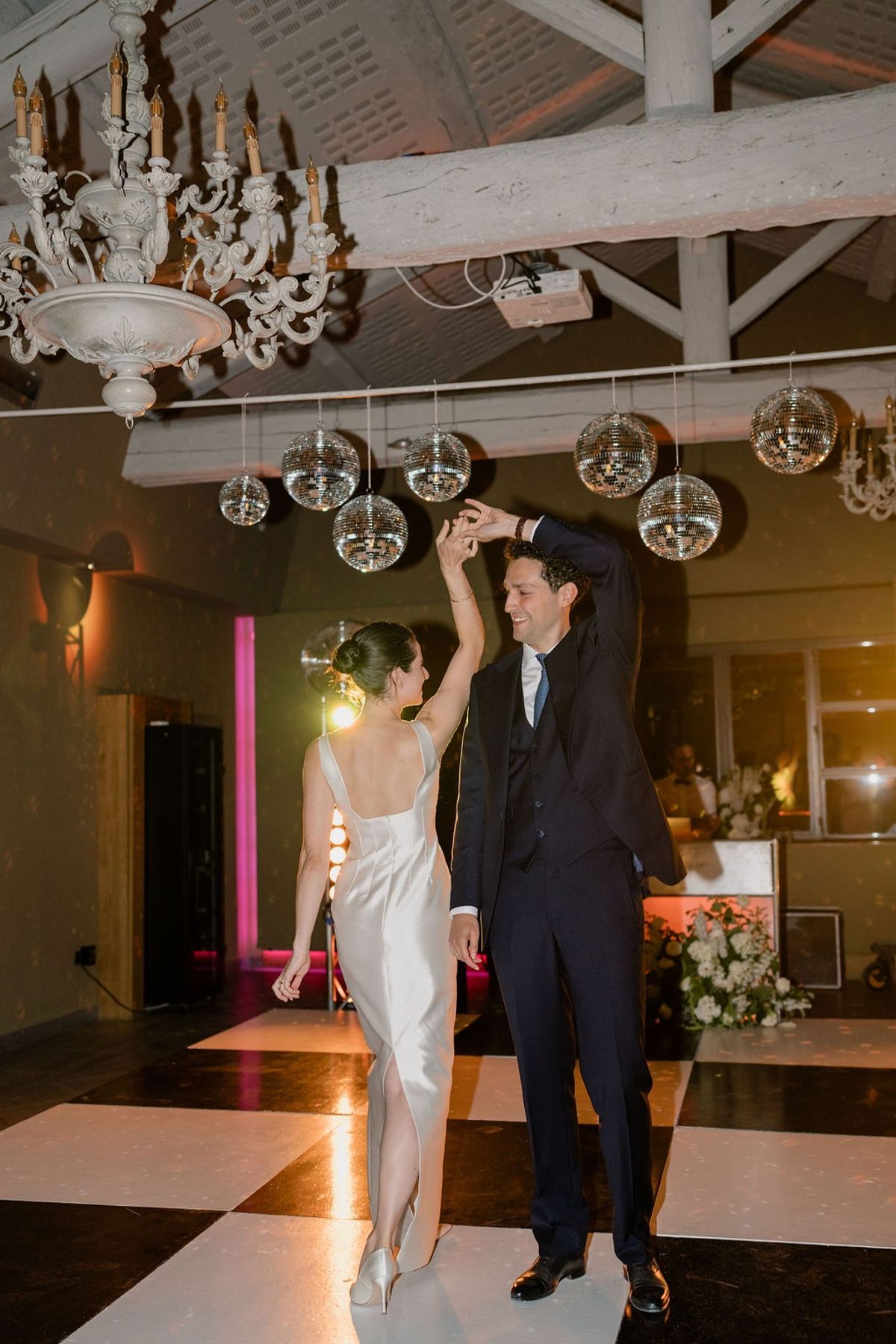 Groom twirling bride under disco balls and chandelier with magenta uplighting