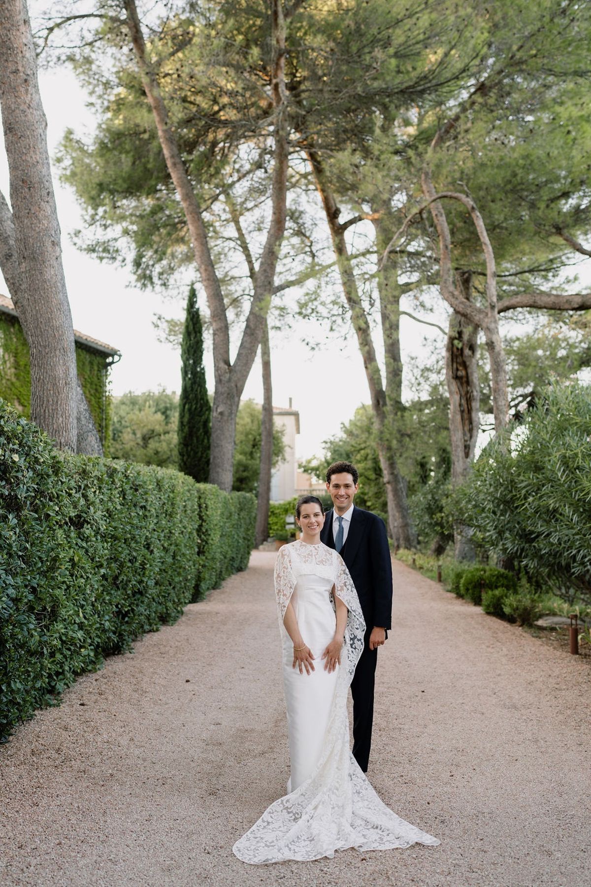 Couple on gravel allee with clipped hedges and umbrella pines in formal attire