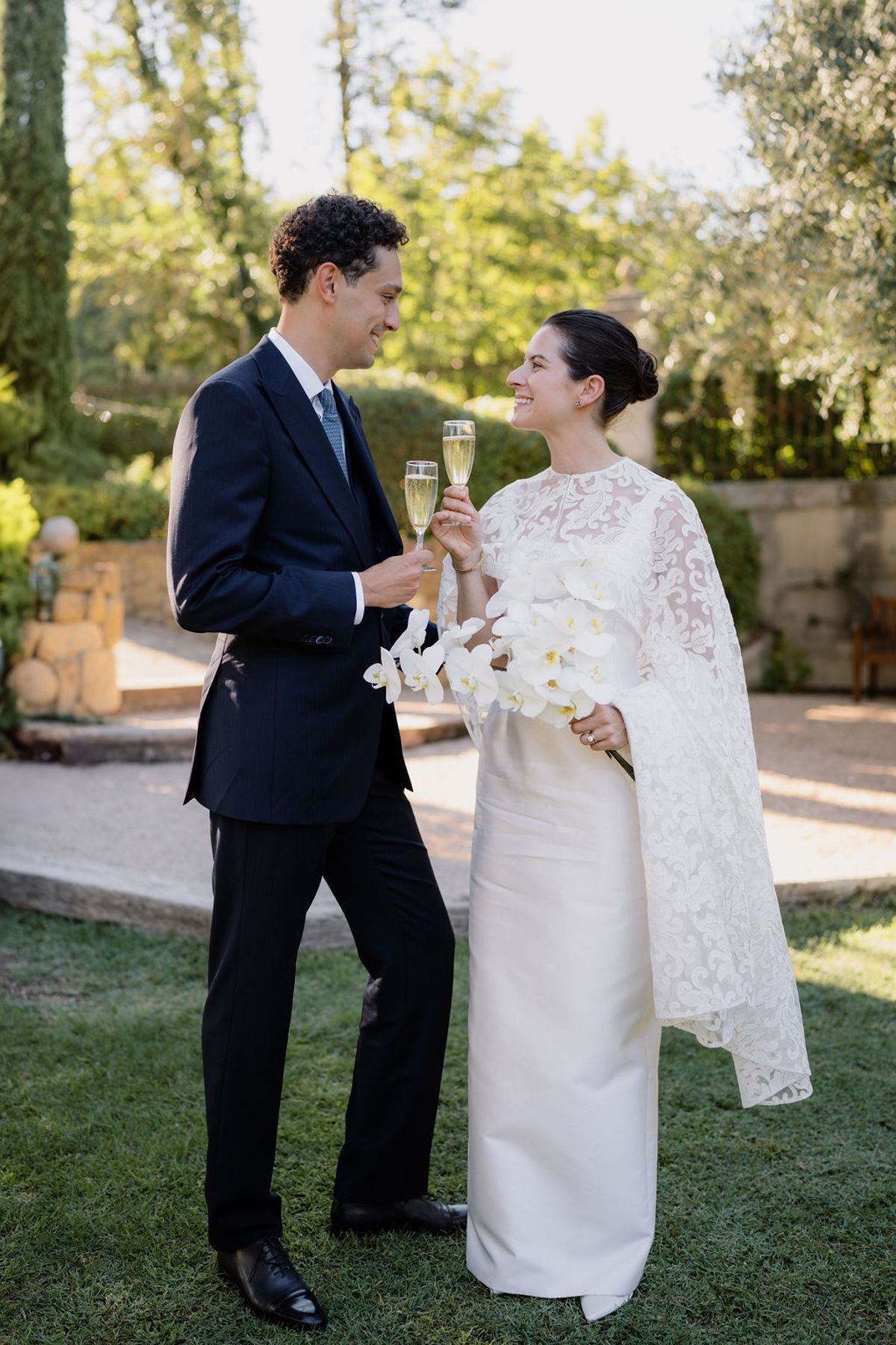 Bride and groom toasting champagne on lawn with orchid bouquet smiling