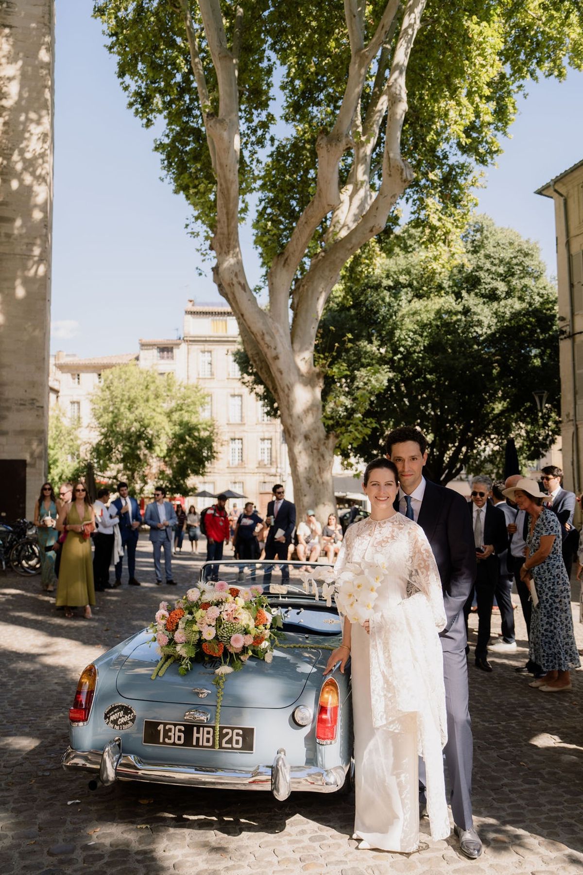 Couple beside powder-blue vintage convertible with blush floral arrangement on boot