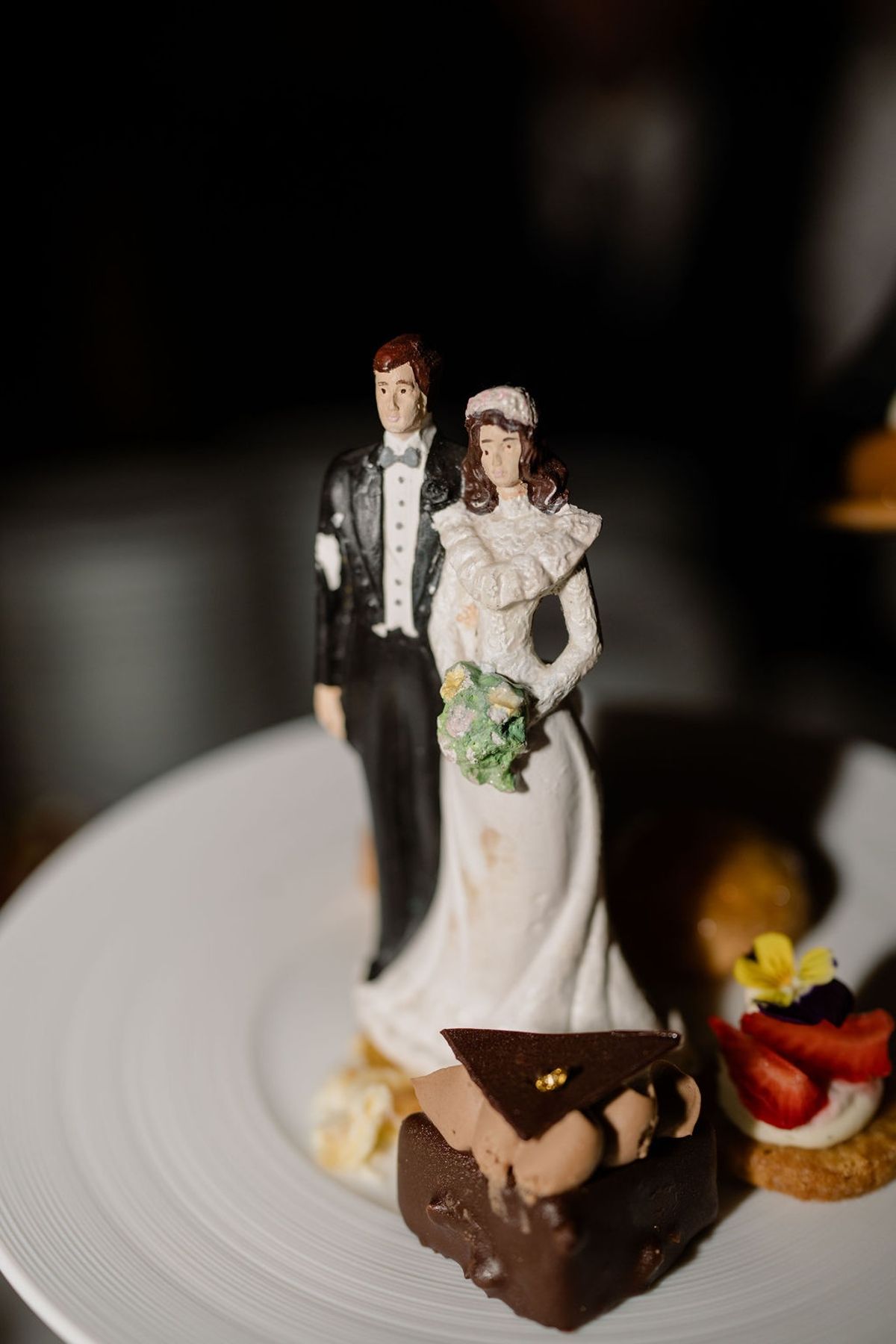 Hand-painted vintage couple cake topper on plate beside chocolate dessert and petit four