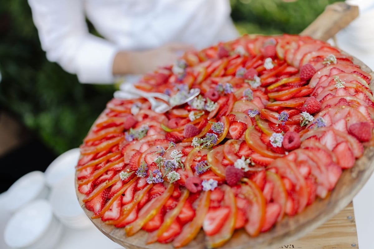 Waiter holding wooden platter with concentric strawberry fig and citrus rings