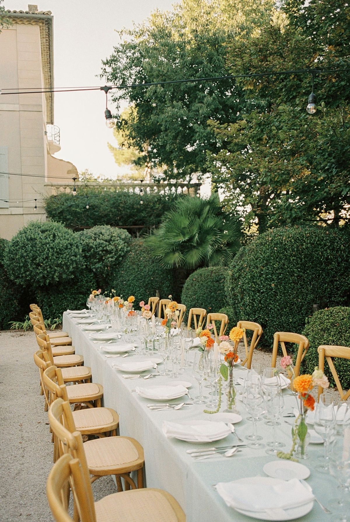 Long sage-linen dinner table with woven chairs and coral blush bud-vase runner