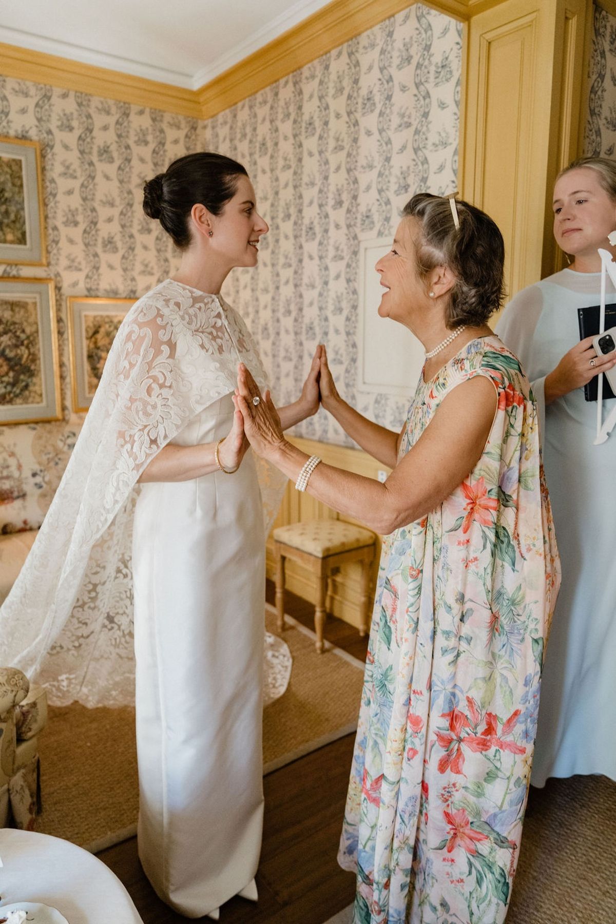 Bride sharing tender hands-clasped moment with mother in chateau bedroom