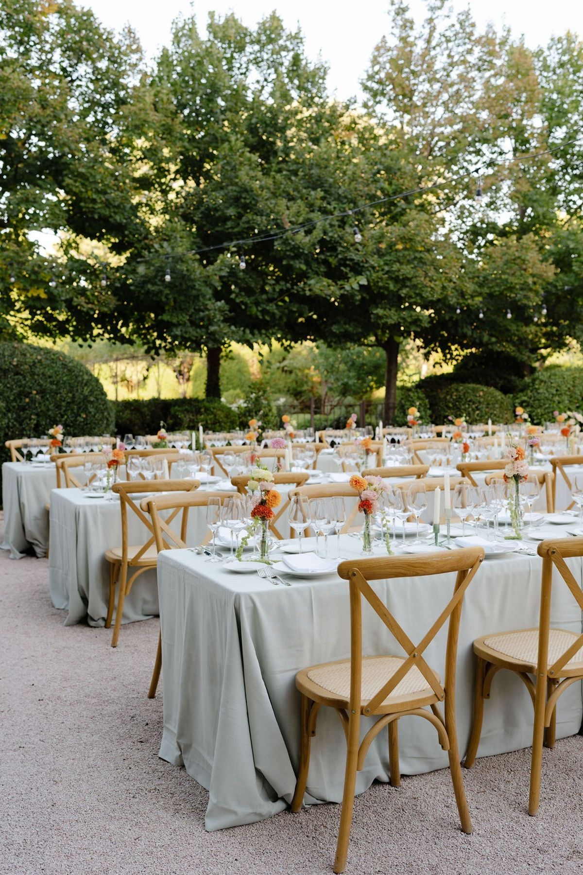 Long sage linen banquet table with bistro chairs and coral-blush bud-vase florals