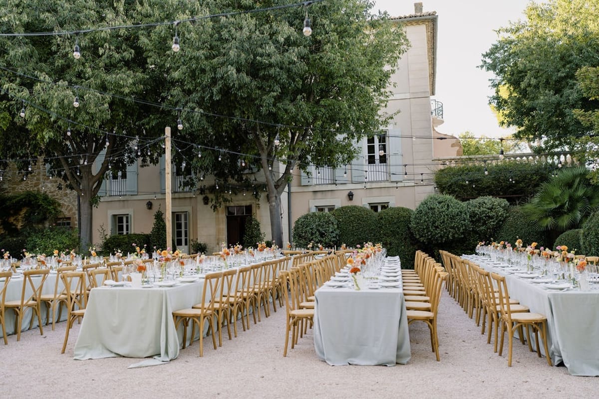 Symmetrical view of long dinner tables under bistro lights with honey-stone chateau