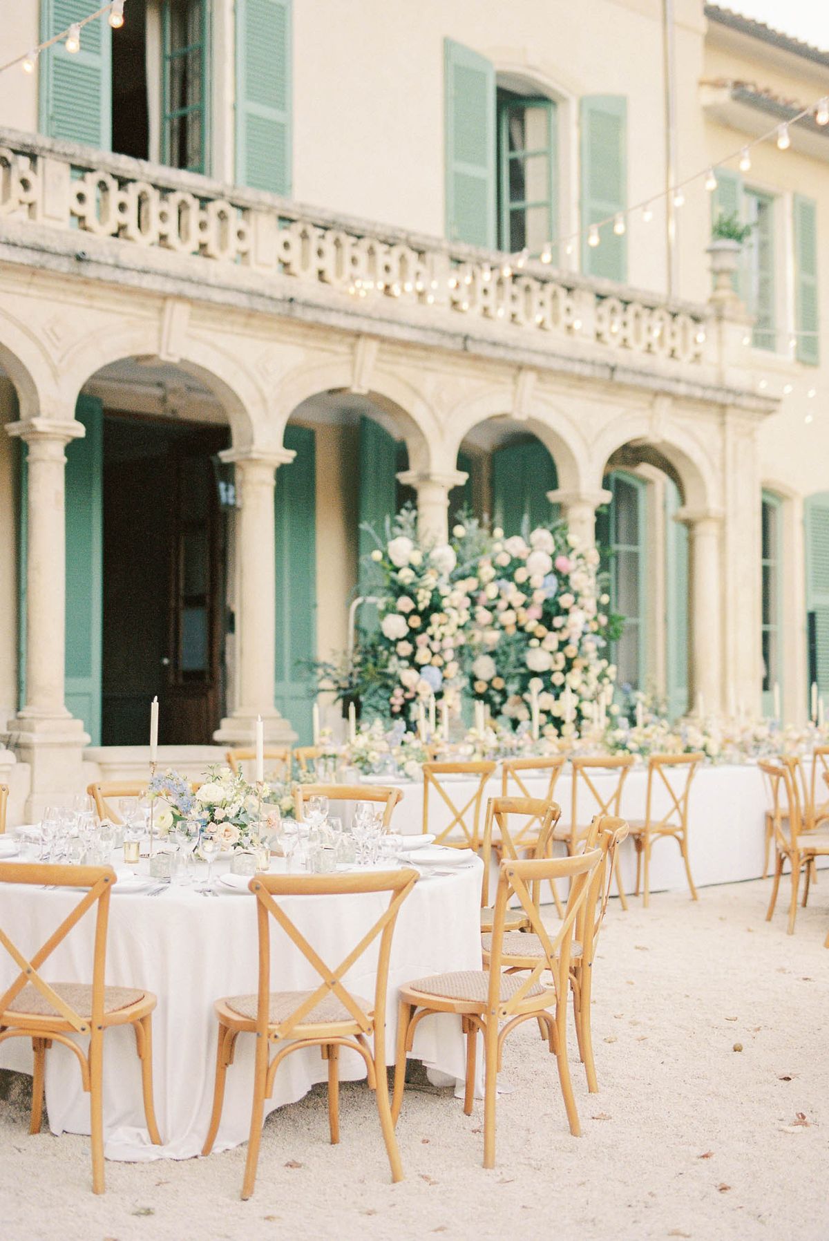 Round table with dusty blue and blush florals before head table with floral installation at teal-shuttered chateau