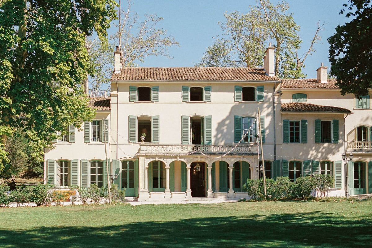 Provencal manor house with cream facades, terracotta roof, sage green shutters, and arched colonnade entrance
