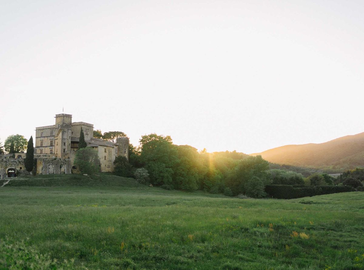 Honey limestone chateau with square tower and cypress trees backlit by setting sun across open field