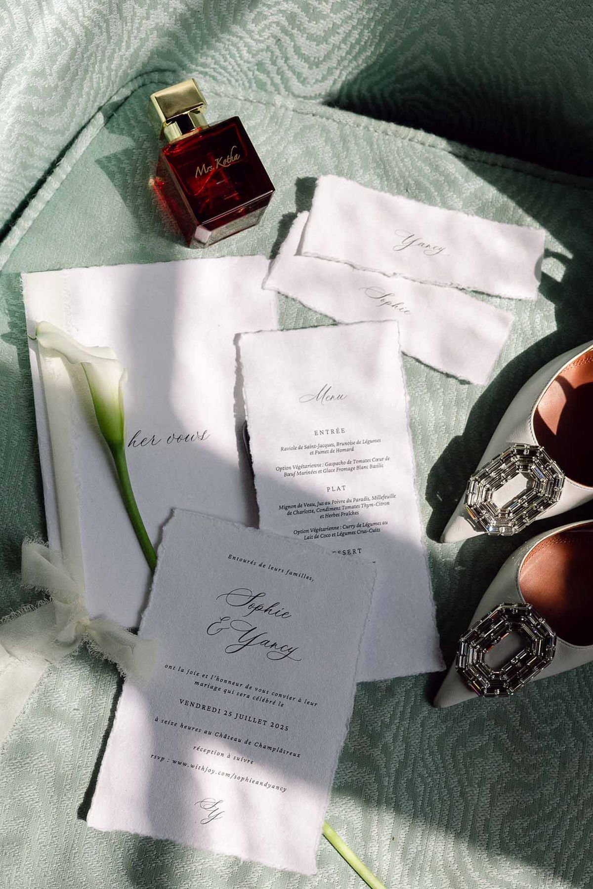 Stationery suite with pale blue invitation, vow booklet, crystal-toe heels, and calla lily on sage moire fabric