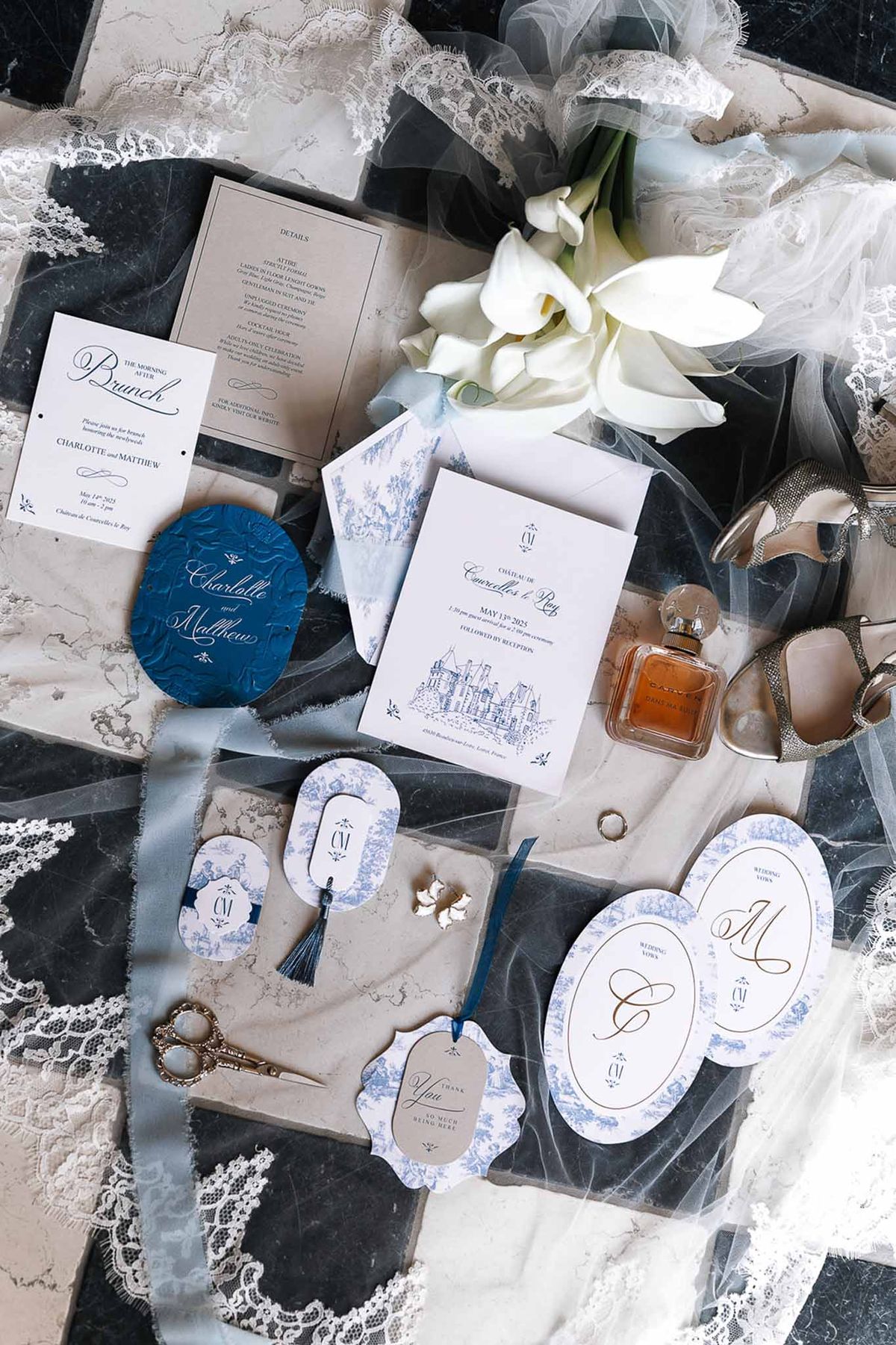 Wedding stationery suite in blue toile de Jouy with calla lilies, tulle veil, silver heels, and perfume on dark marble