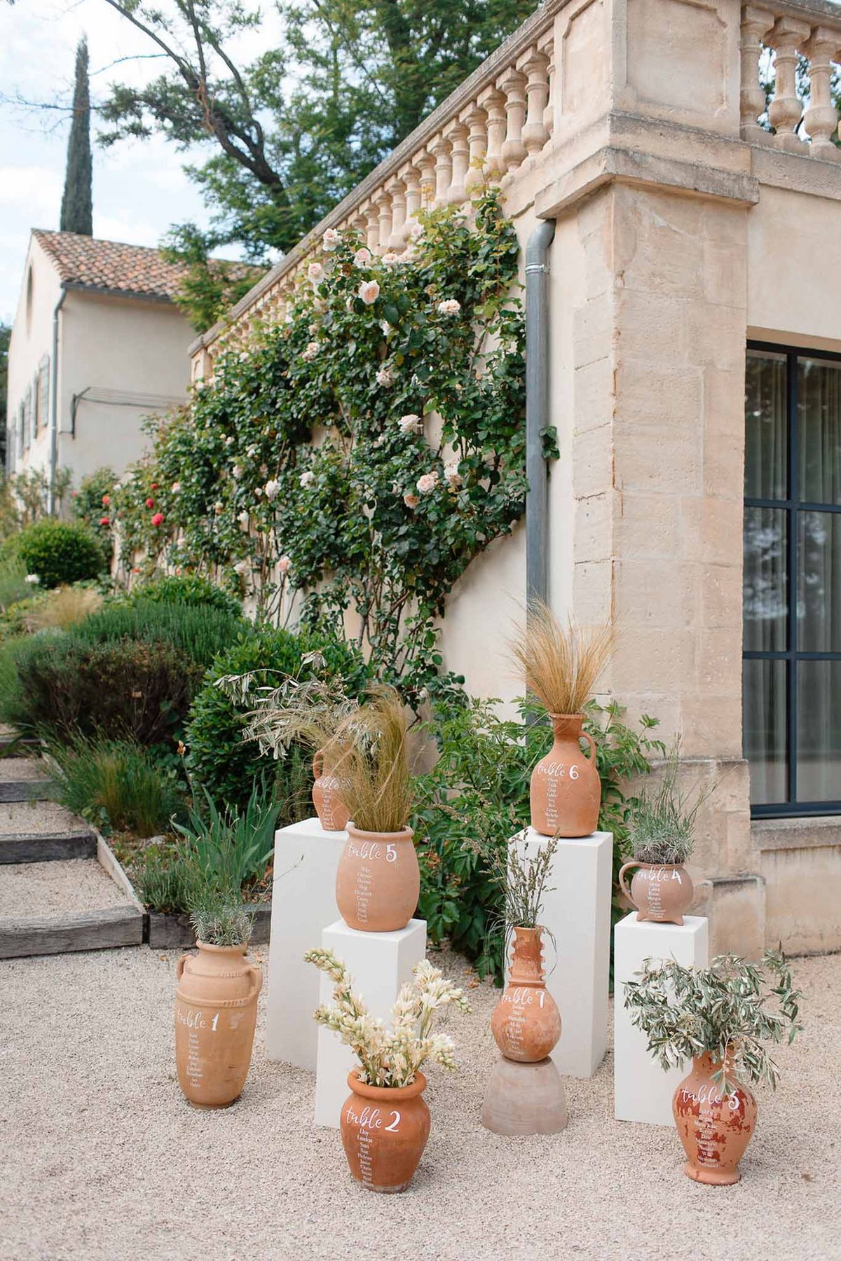 Eight terracotta amphora seating plan pots with calligraphy and dried botanicals at chateau terrace