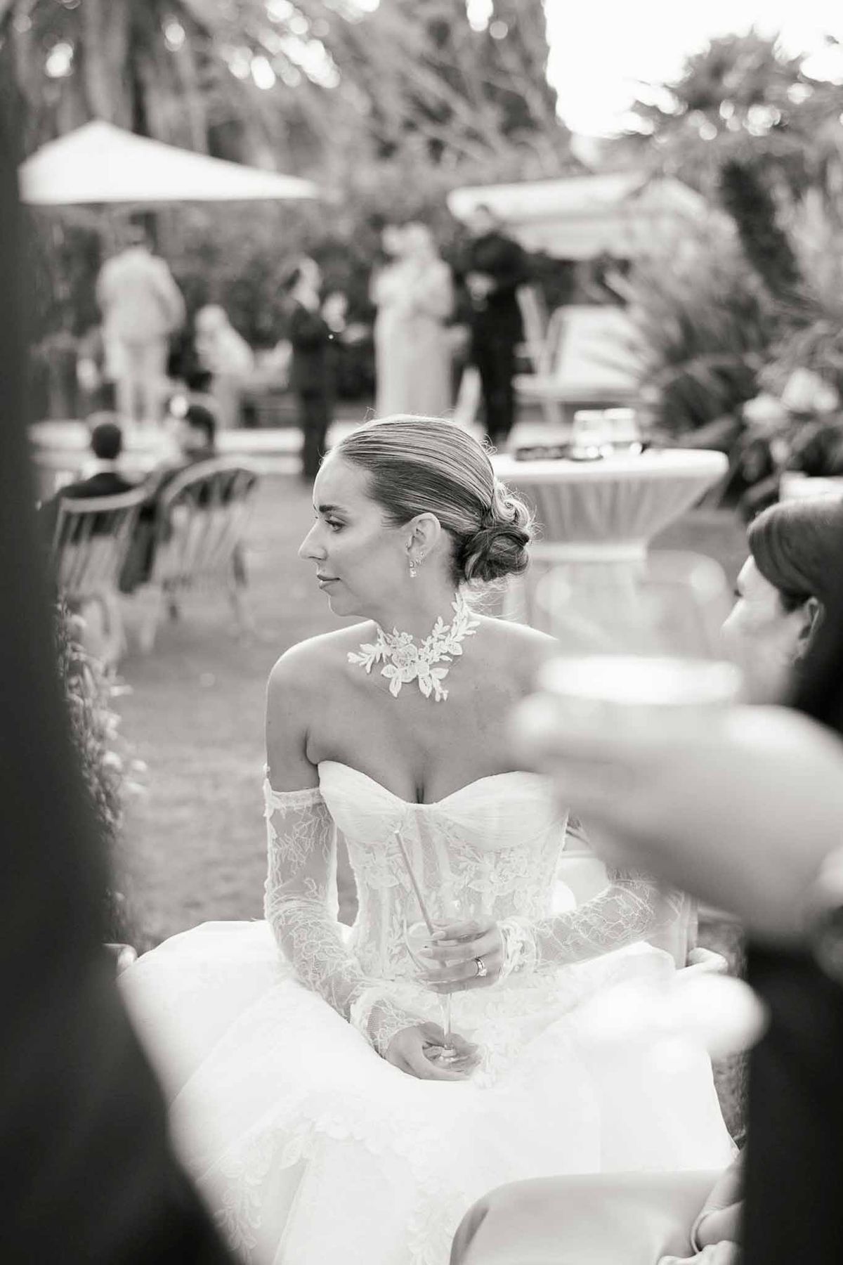 Black-and-white portrait of bride in strapless gown with lace gloves holding champagne during cocktail hour
