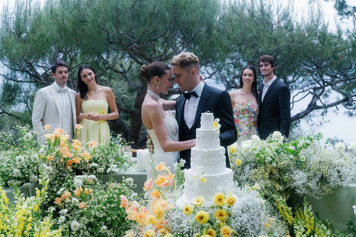 Couple and bridal party at five-tier cake with yellow ranunculus and peach tulip garden display