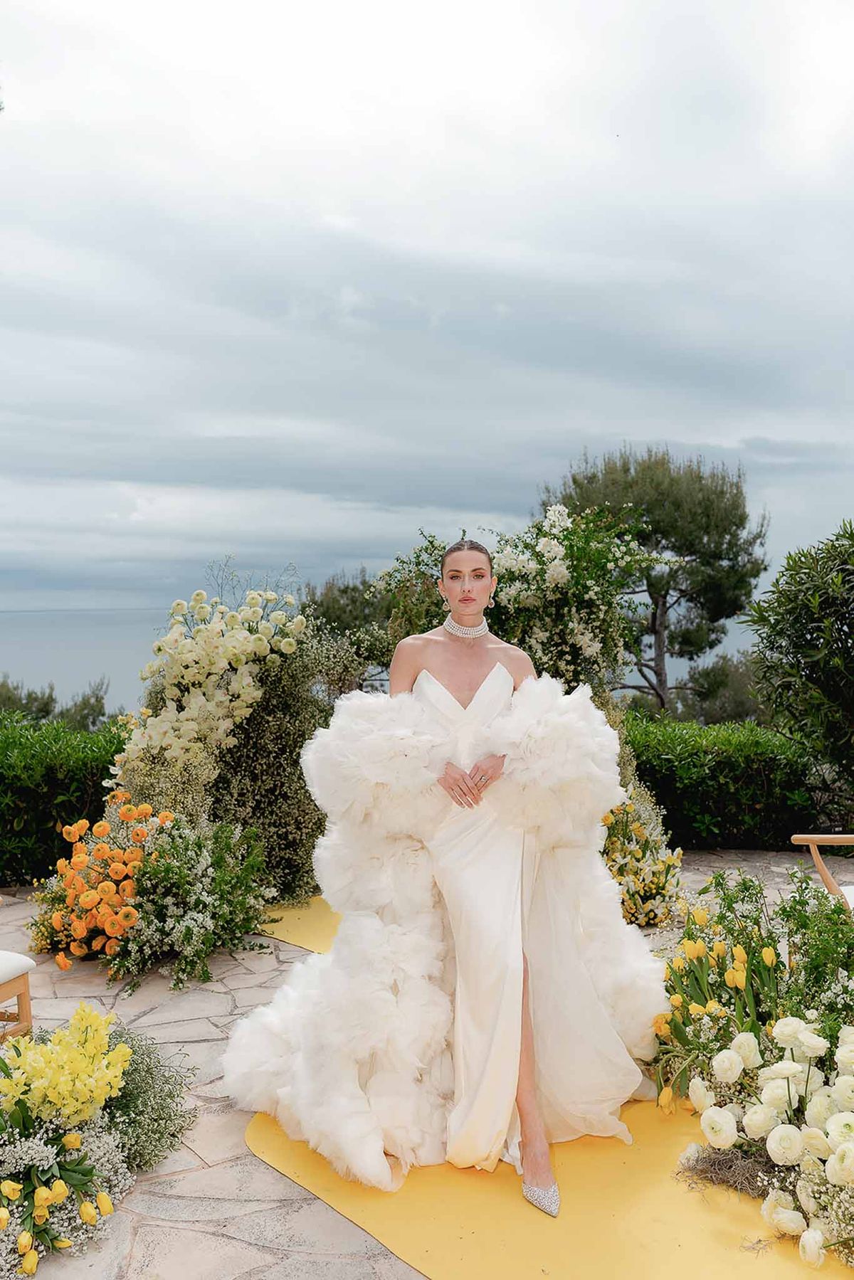 Bride in ruffled tulle overskirt on yellow runner surrounded by orange ranunculus and yellow tulip arc