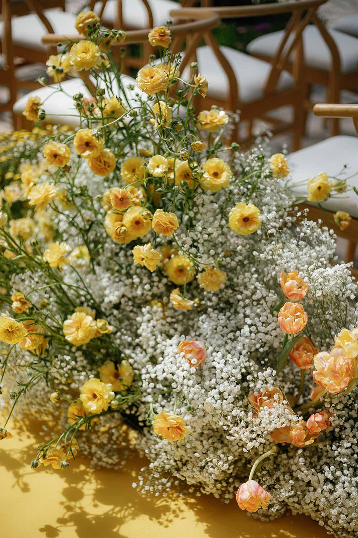 Floral arrangement of white baby's breath, yellow ranunculus, and peach parrot tulips on yellow surface