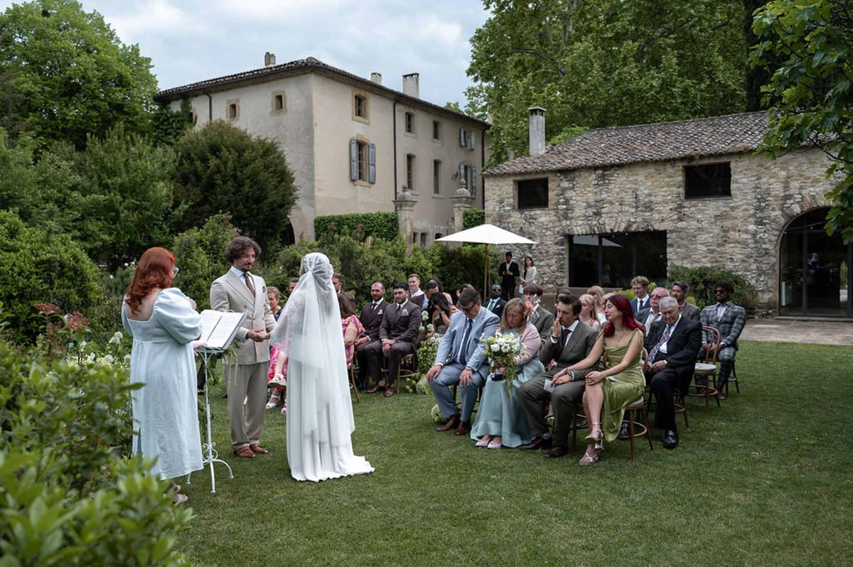 Outdoor lawn ceremony before country estate with blue shutters and guests on bistro chairs
