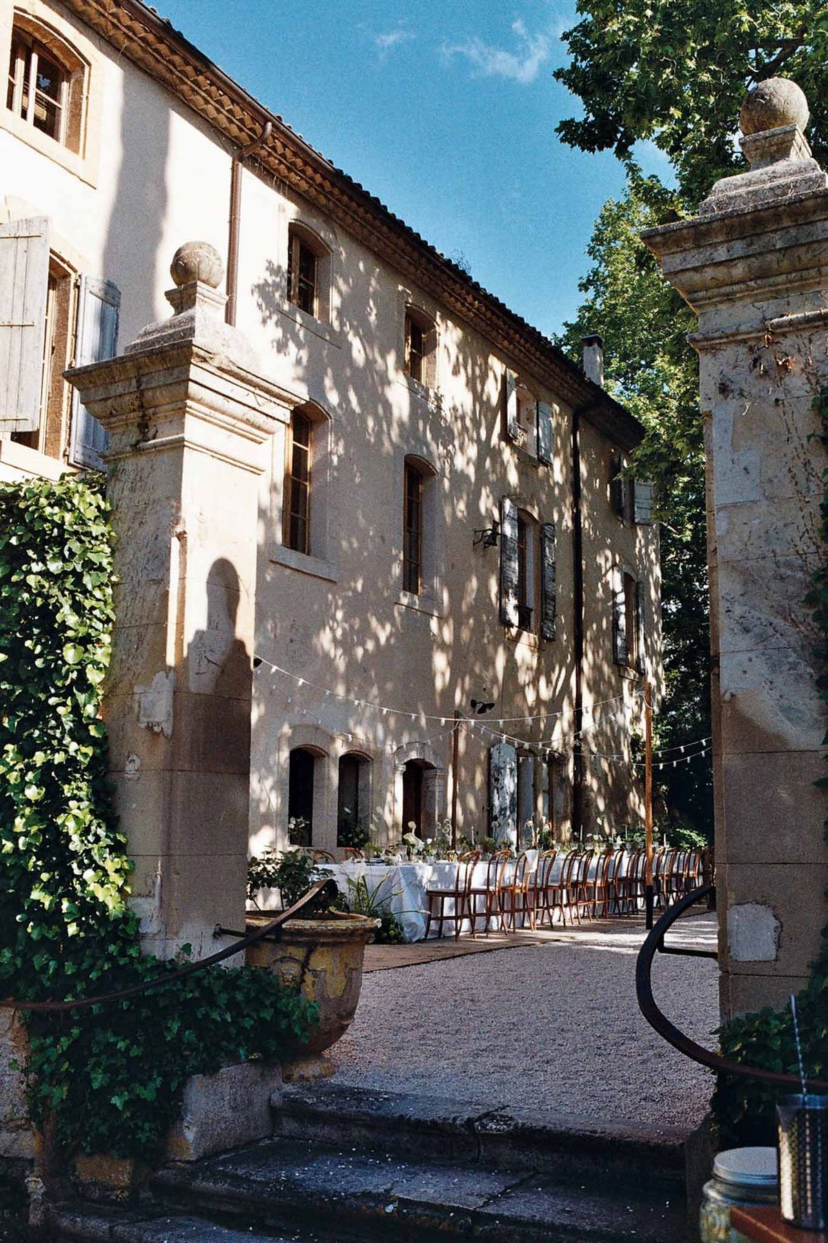 Long banquet table with white linen and bistro chairs set for alfresco dinner at stone bastide