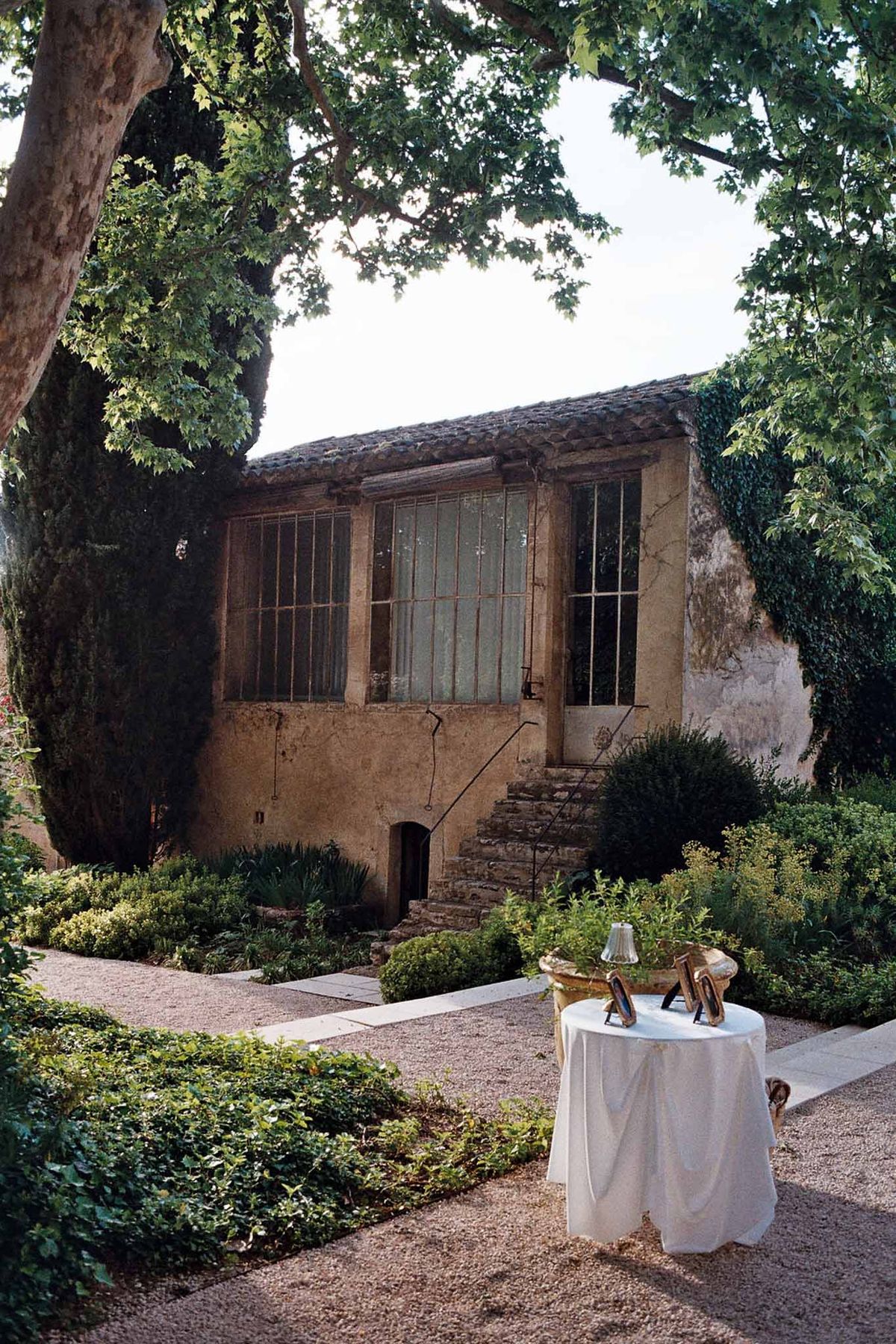 Cocktail hour setup with white-draped high-top table on gravel courtyard at a Provencal stone mas with climbing ivy