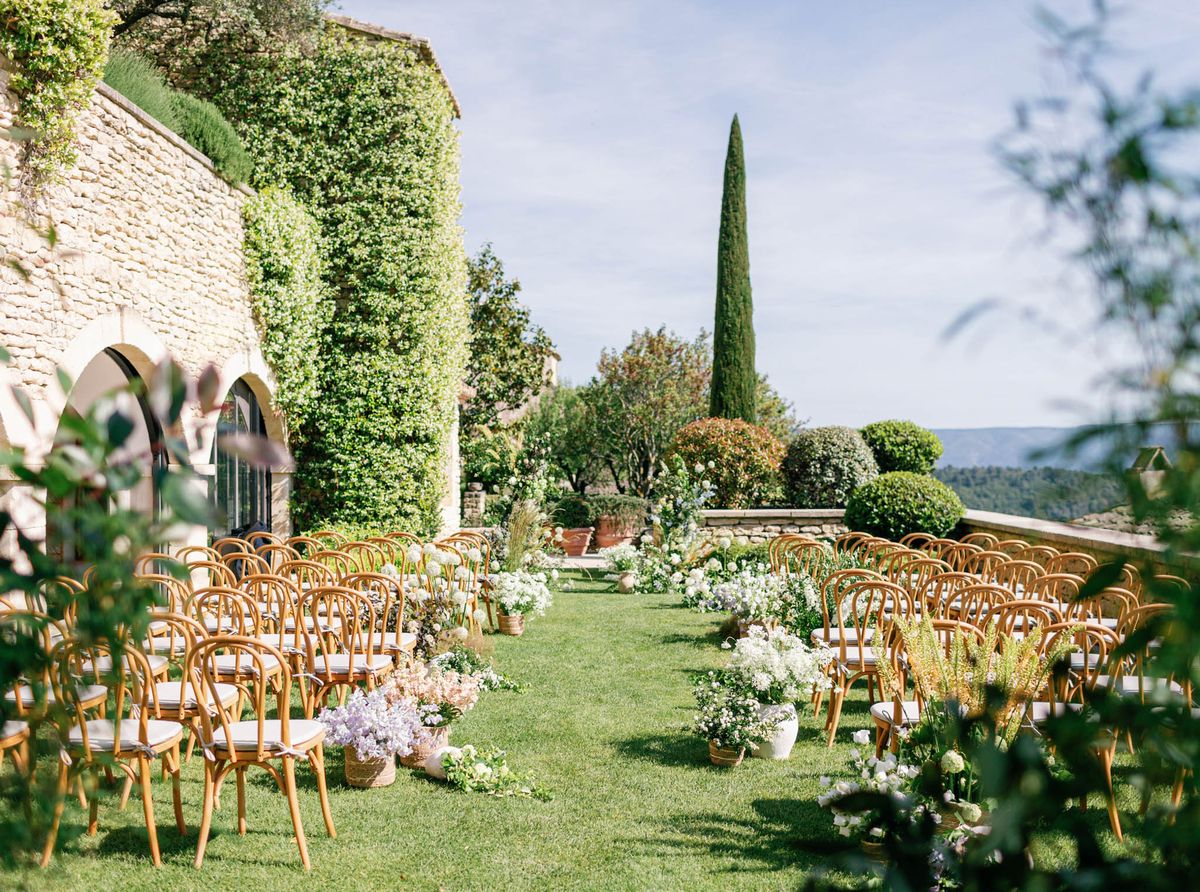 Bentwood chairs on lawn with meadow-style lavender and blush aisle flowers beside ivy-covered Provencal mas