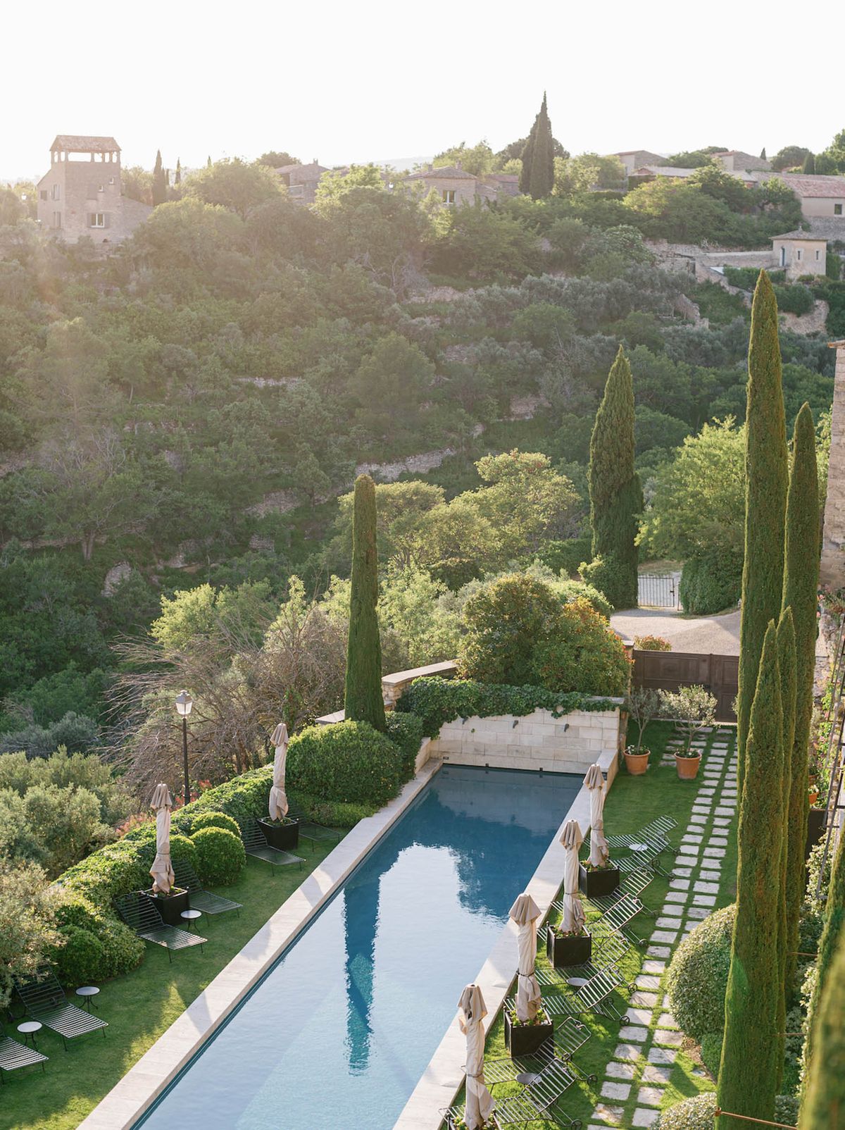 Elevated view of lap pool with cypress trees, topiary planters, and Provencal hilltop village beyond