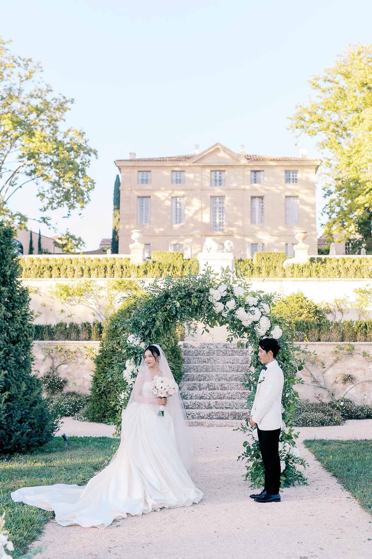 Outdoor ceremony setup with greenery arch and château façade at Château de la Gaude
