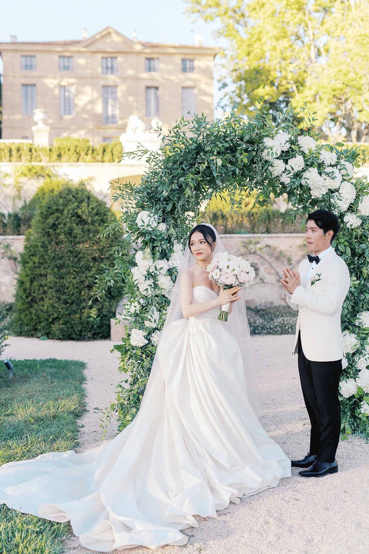 Bride and groom standing under greenery ceremony arch at Château de la Gaude