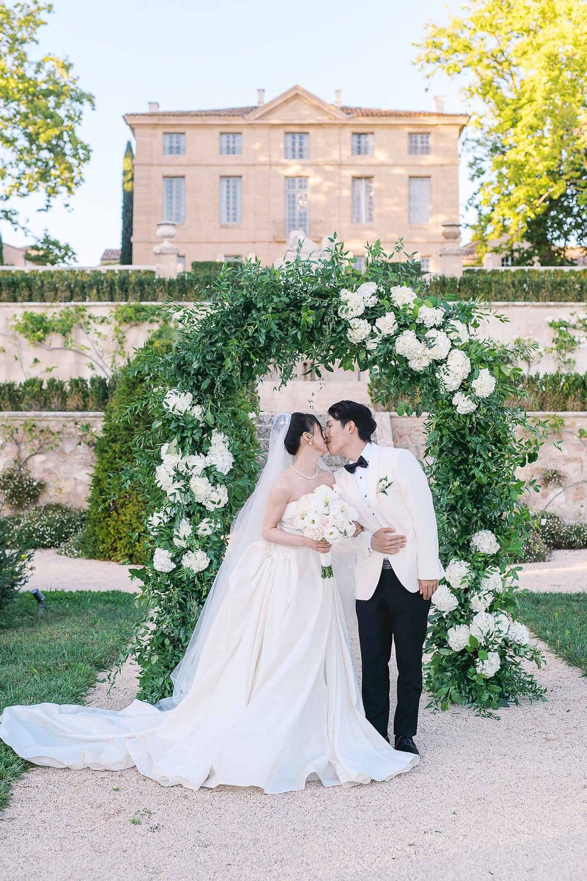 Bride and groom kissing under greenery arch at Château de la Gaude ceremony