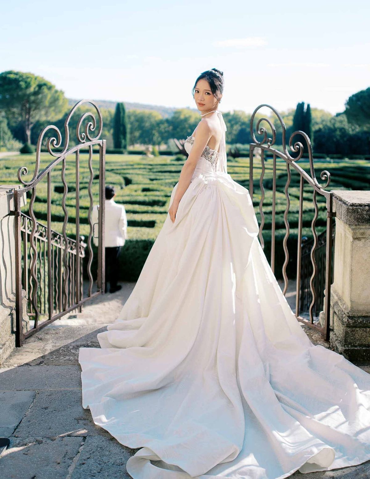 Bride looking over shoulder at garden gate with parterre hedges at Château de la Gaude