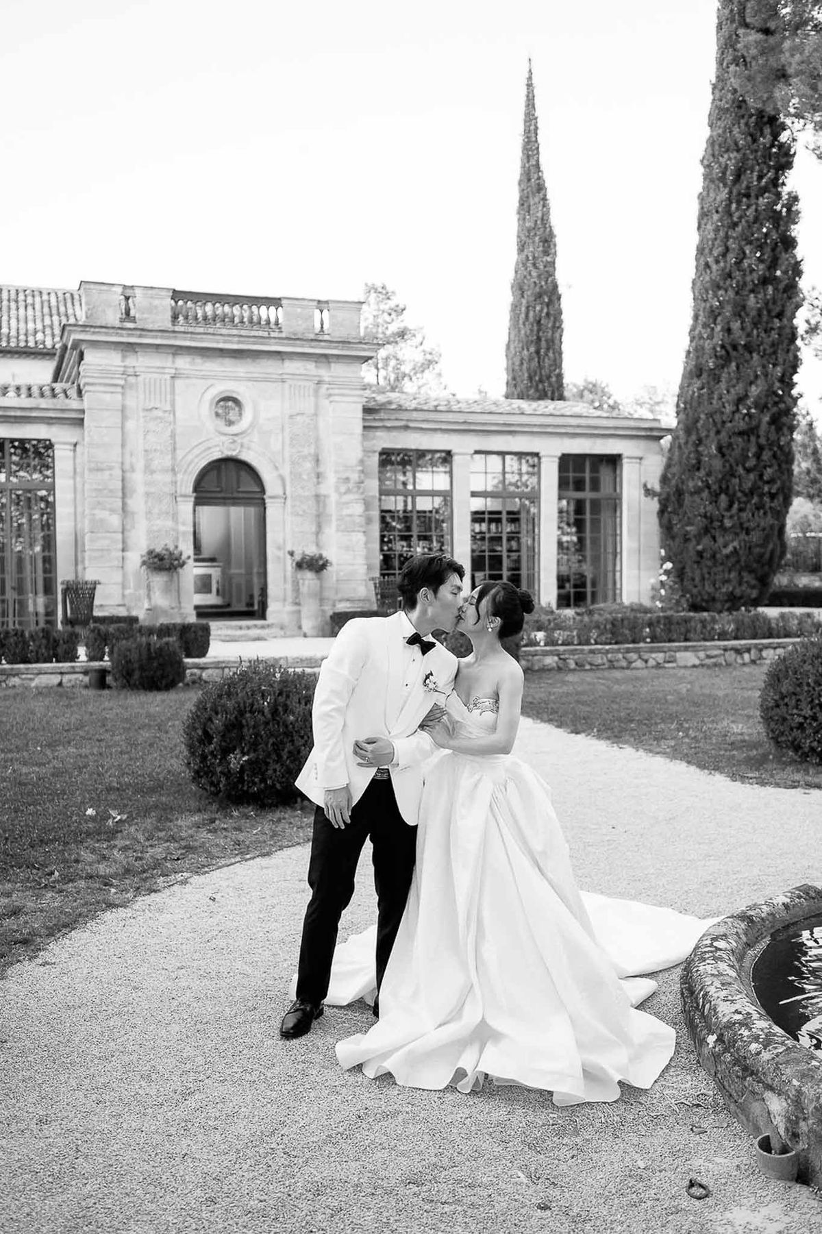 Couple kissing by vintage fountain with château orangery at Château de la Gaude
