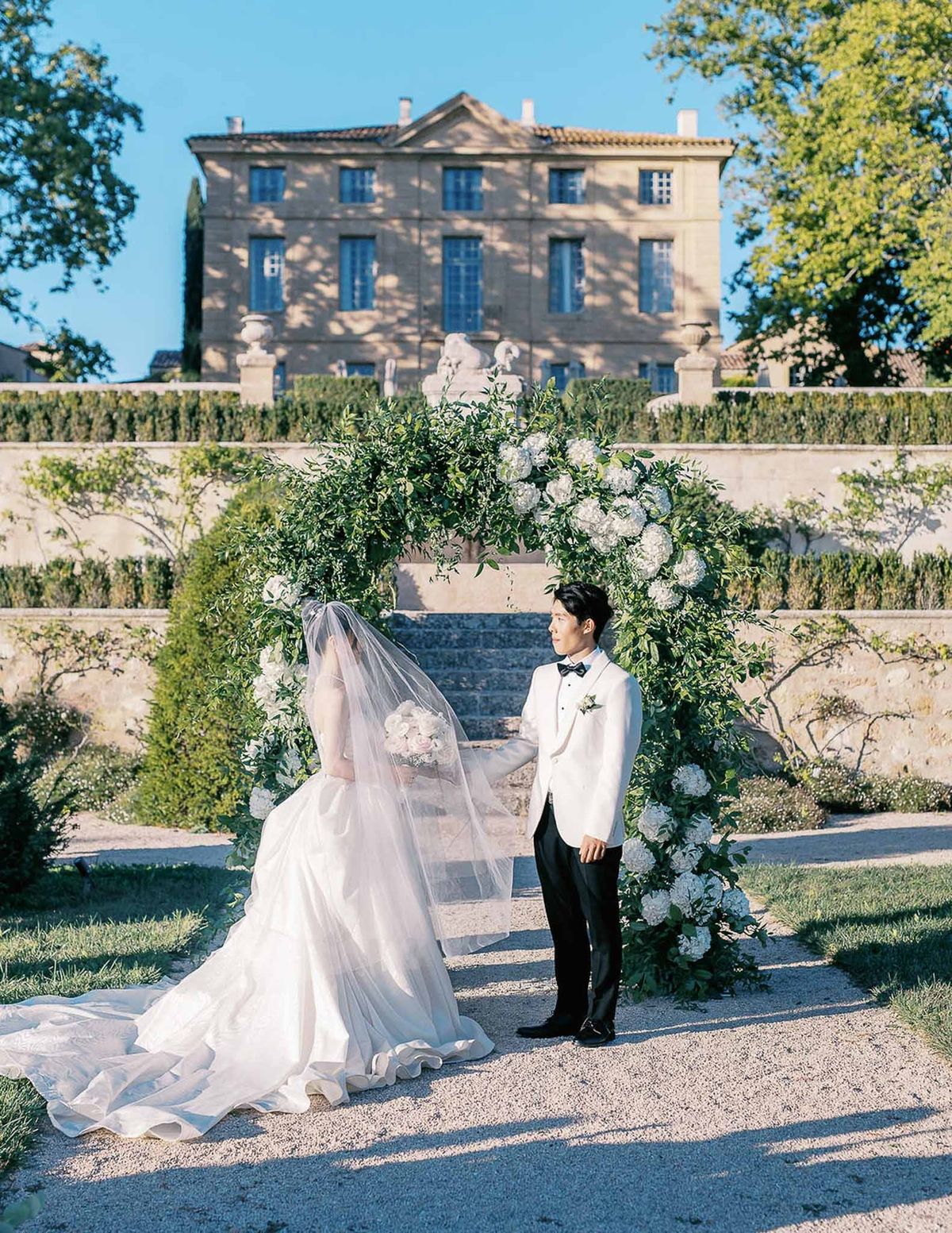 Close-up of couple holding hands under greenery arch at Château de la Gaude ceremony