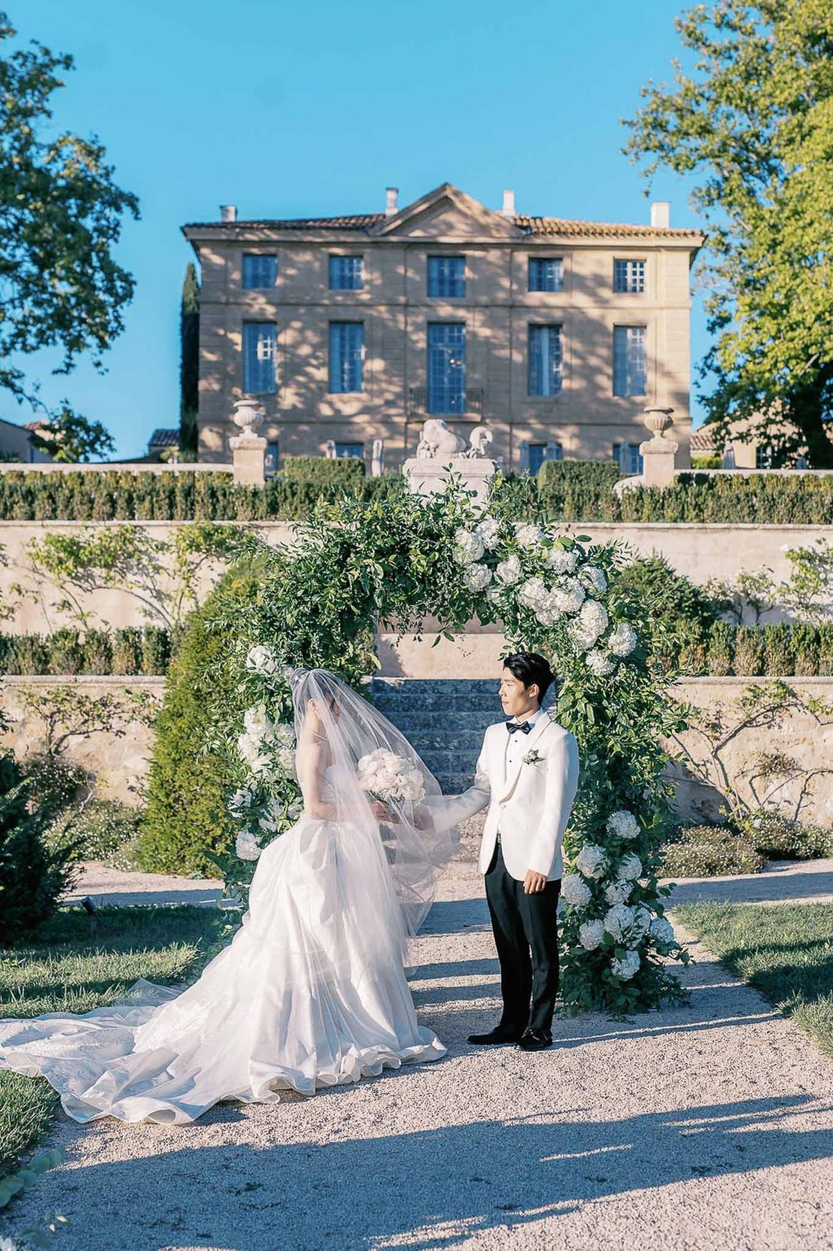 Bride and groom facing each other under ceremony arch at Château de la Gaude