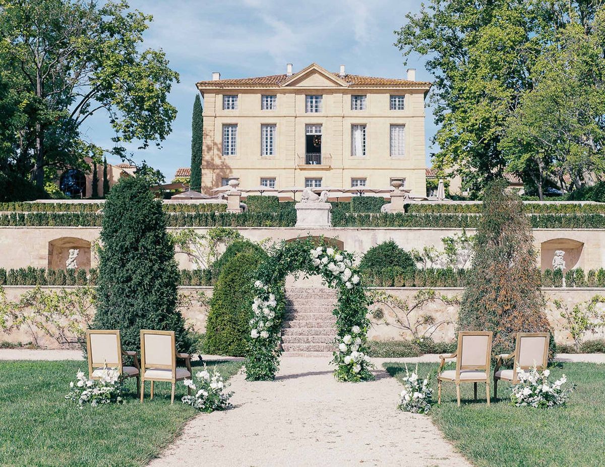 Full ceremony setup with greenery arch, chairs and château façade at Château de la Gaude