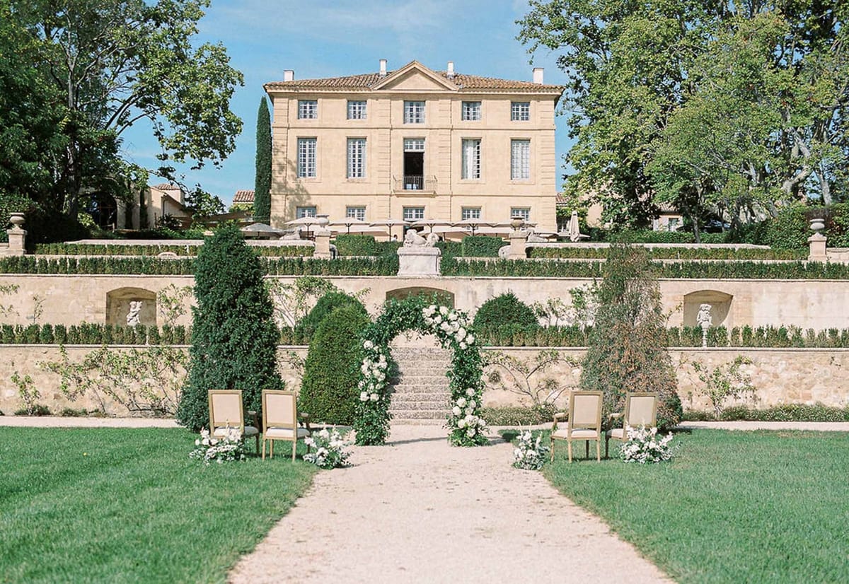 Ceremony setup with greenery arch and topiary leading to Château de la Gaude