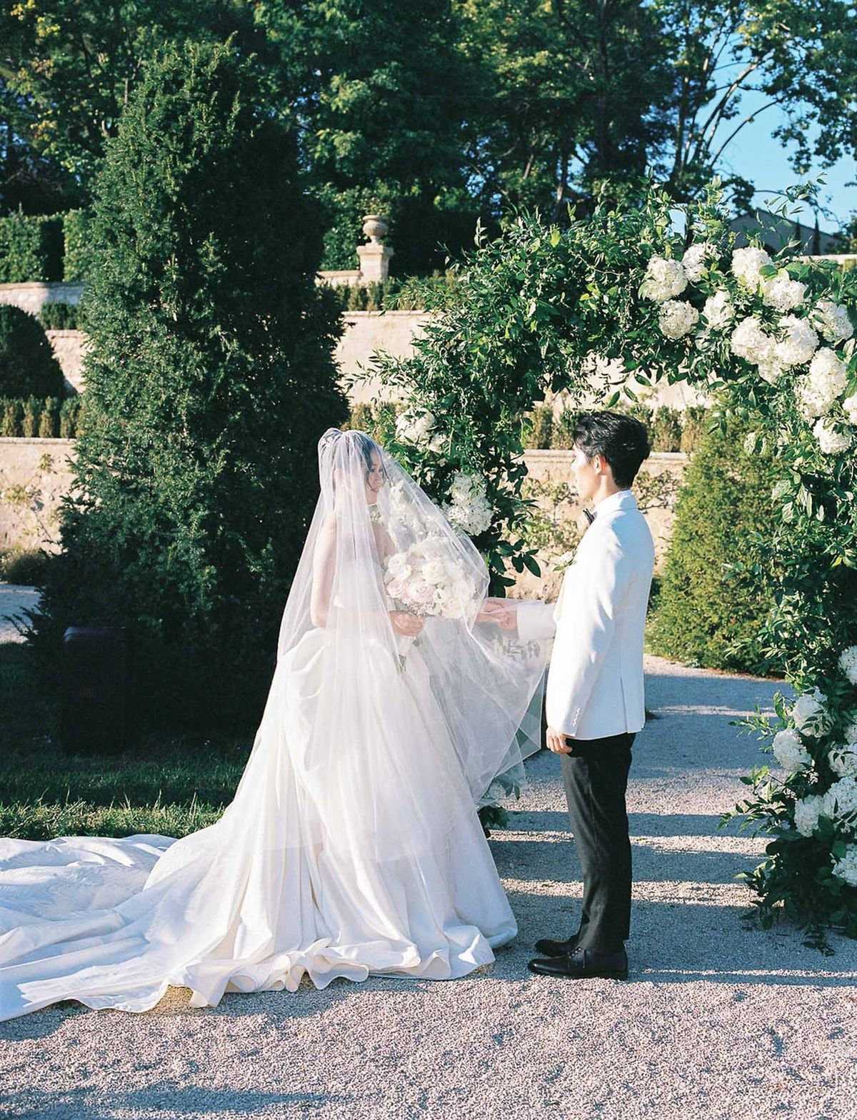 Couple holding hands during vows at greenery arch in golden hour at Château de la Gaude