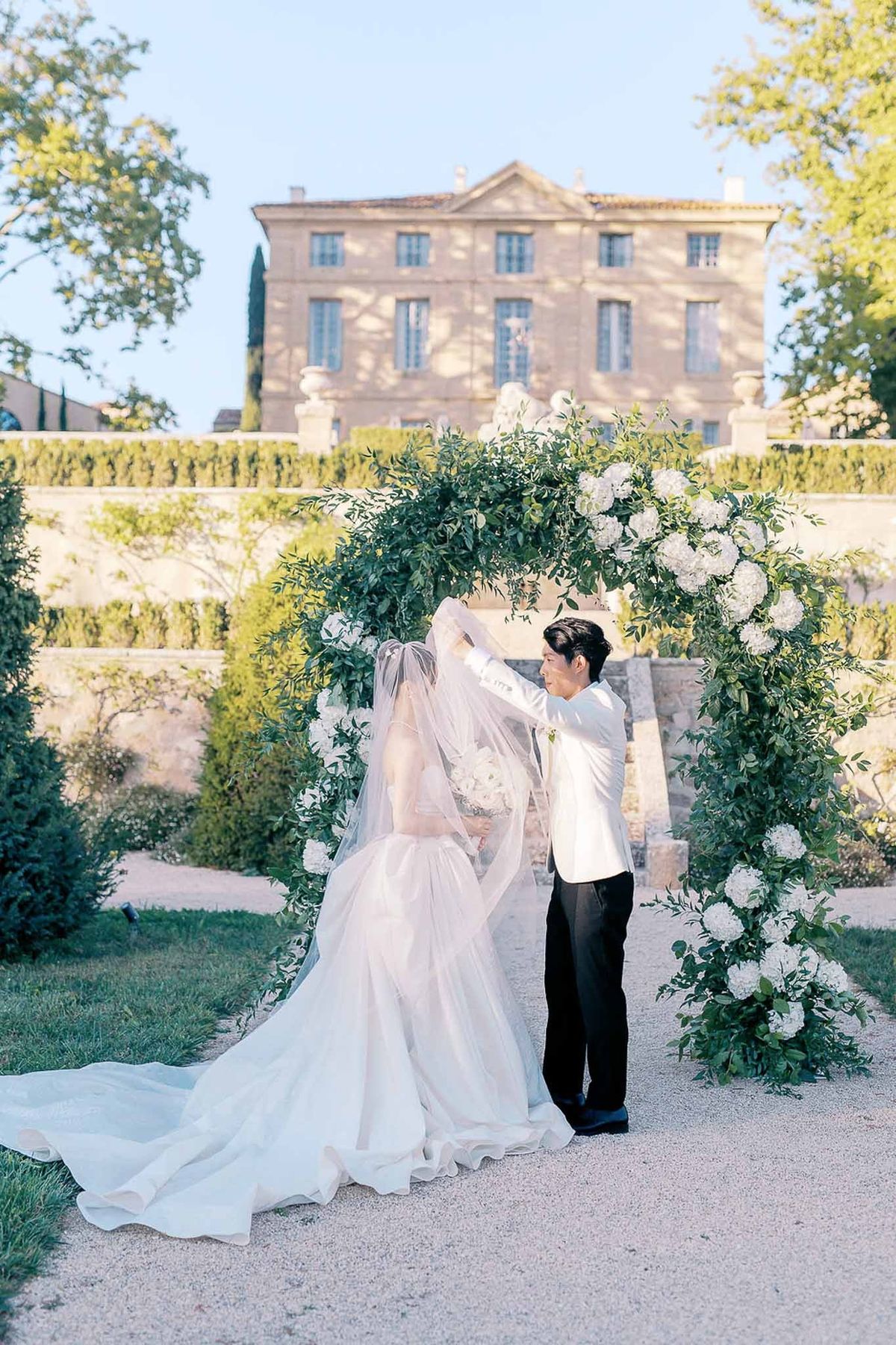 Groom lifting bride's veil for kiss under ceremony arch at sunset at Château de la Gaude
