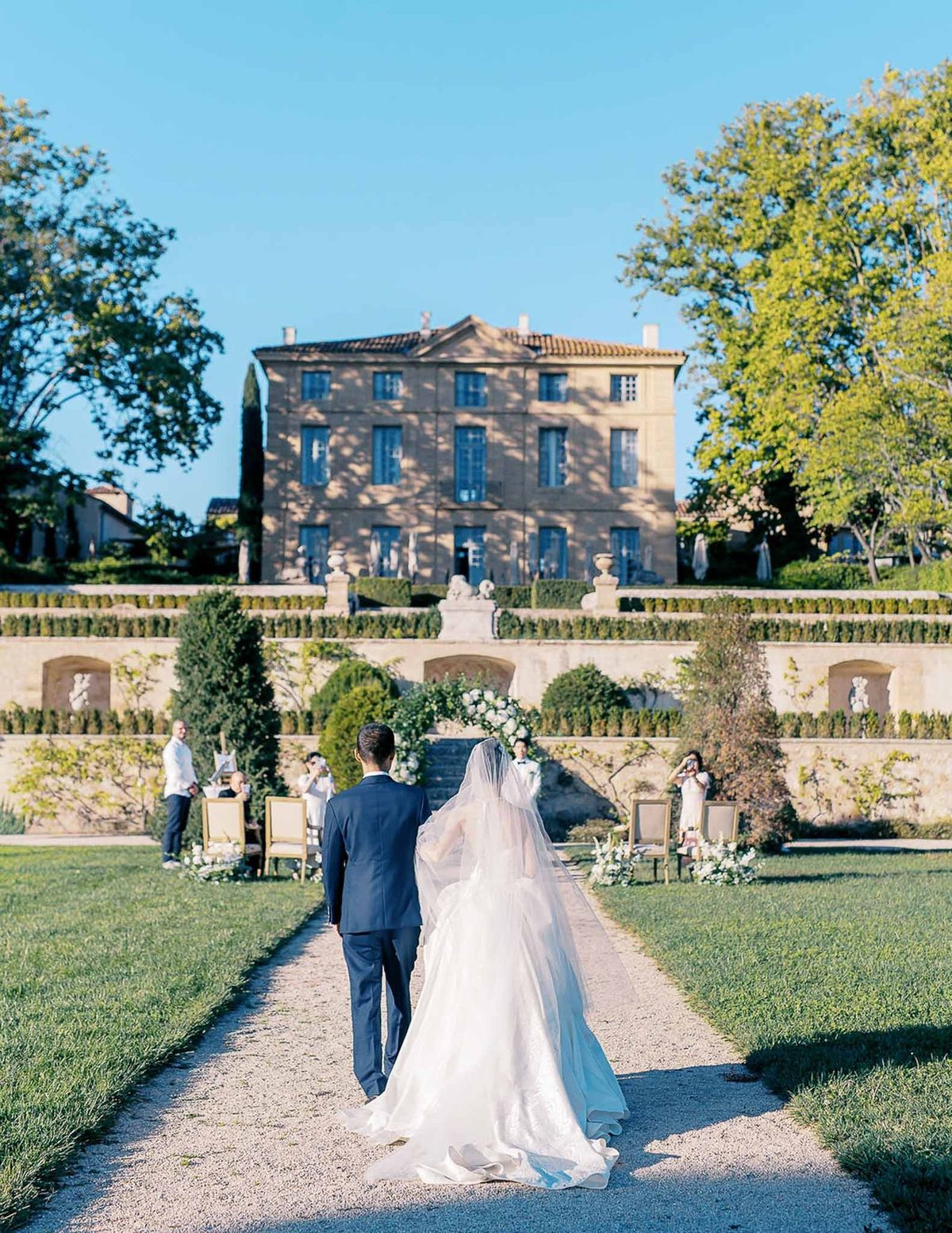 Bride walking down outdoor aisle towards ceremony arch at Château de la Gaude