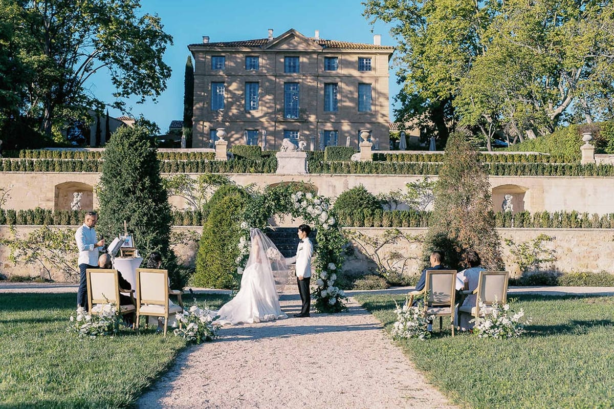 Couple at ceremony arch with officiant and seated guests at Château de la Gaude
