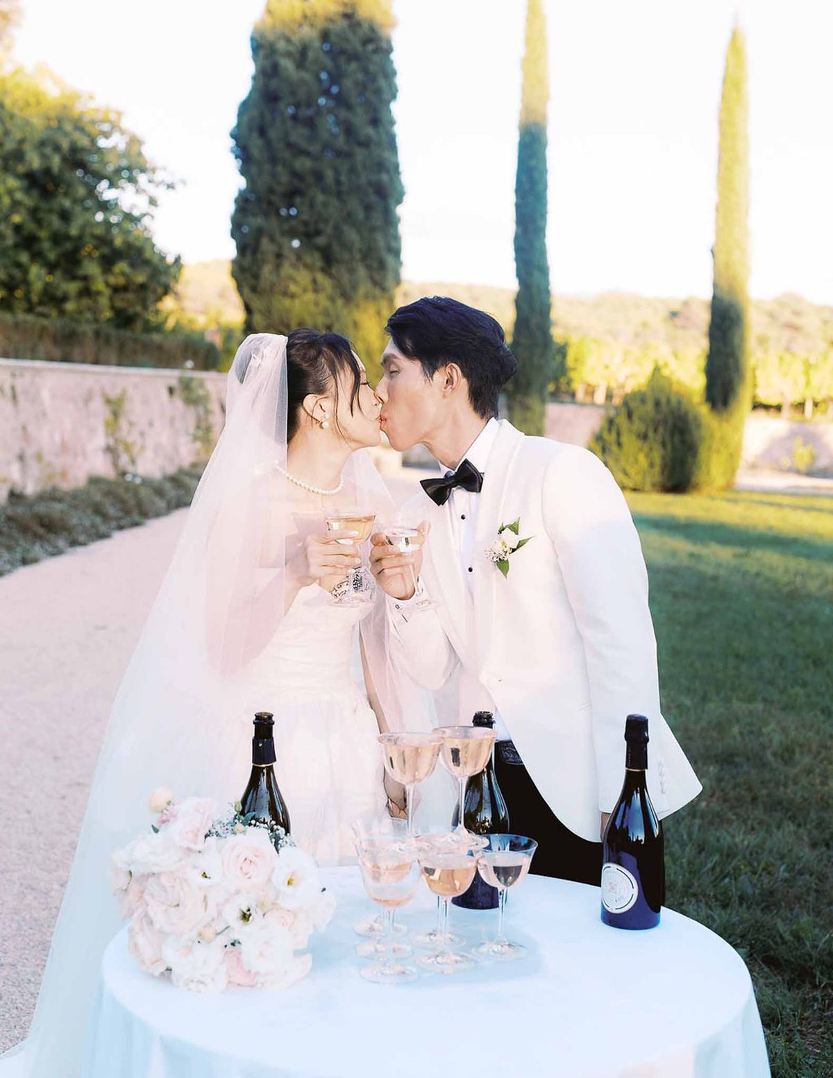 Bride and groom kissing at champagne table with cypress trees at sunset at Château de la Gaude
