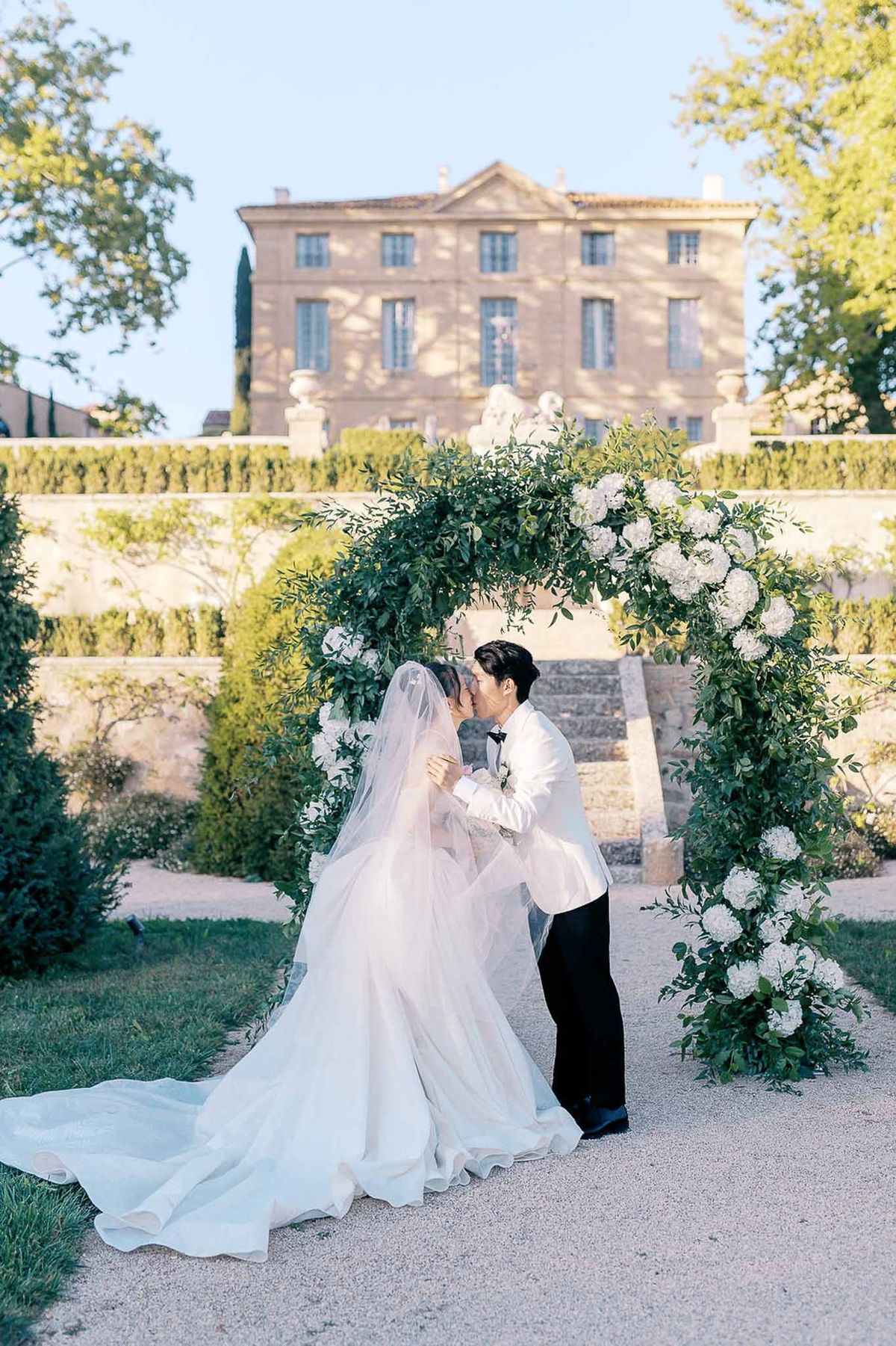 Couple kissing under greenery arch at golden hour at Château de la Gaude