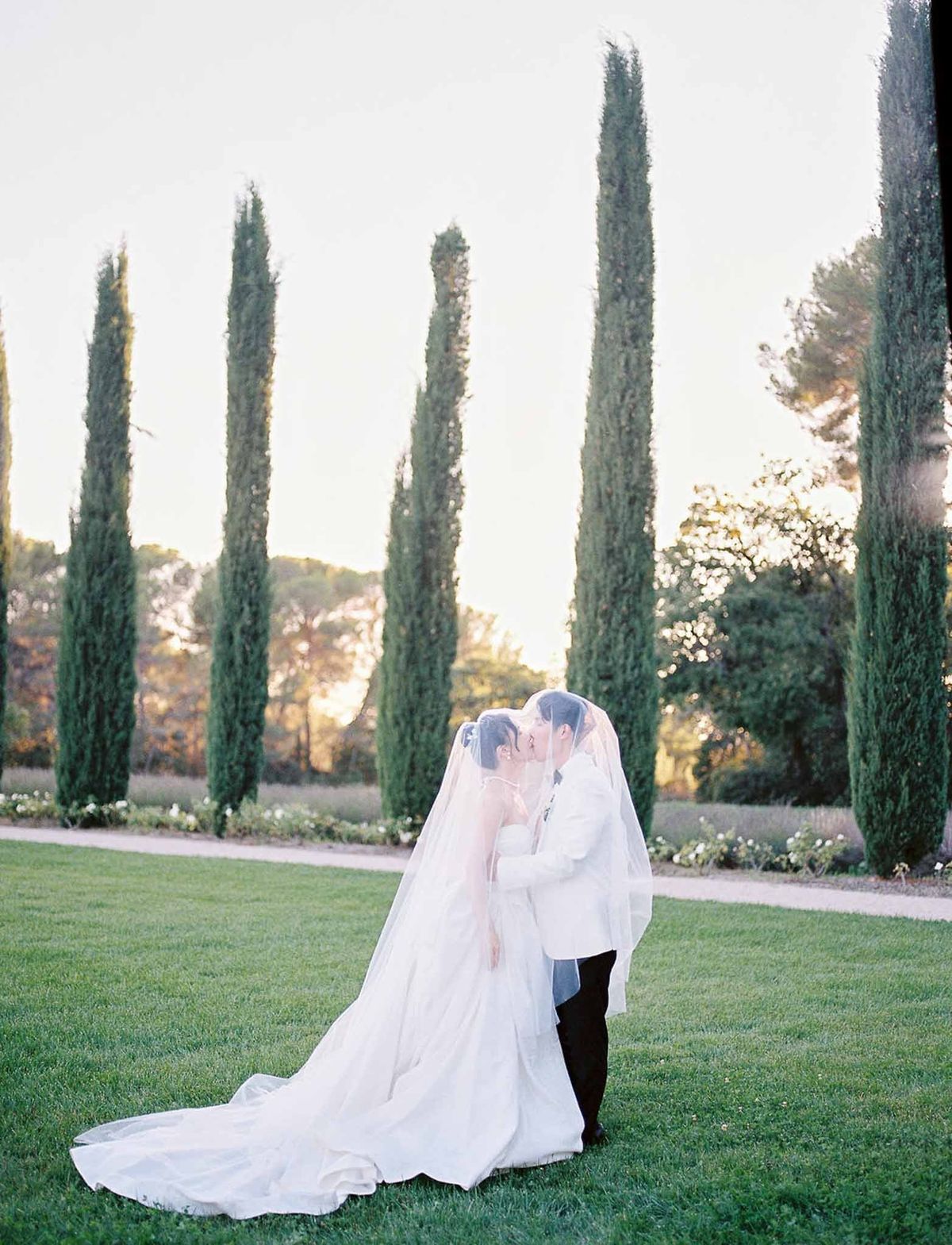 Couple kissing under veil on lawn with cypress trees at sunset at Château de la Gaude