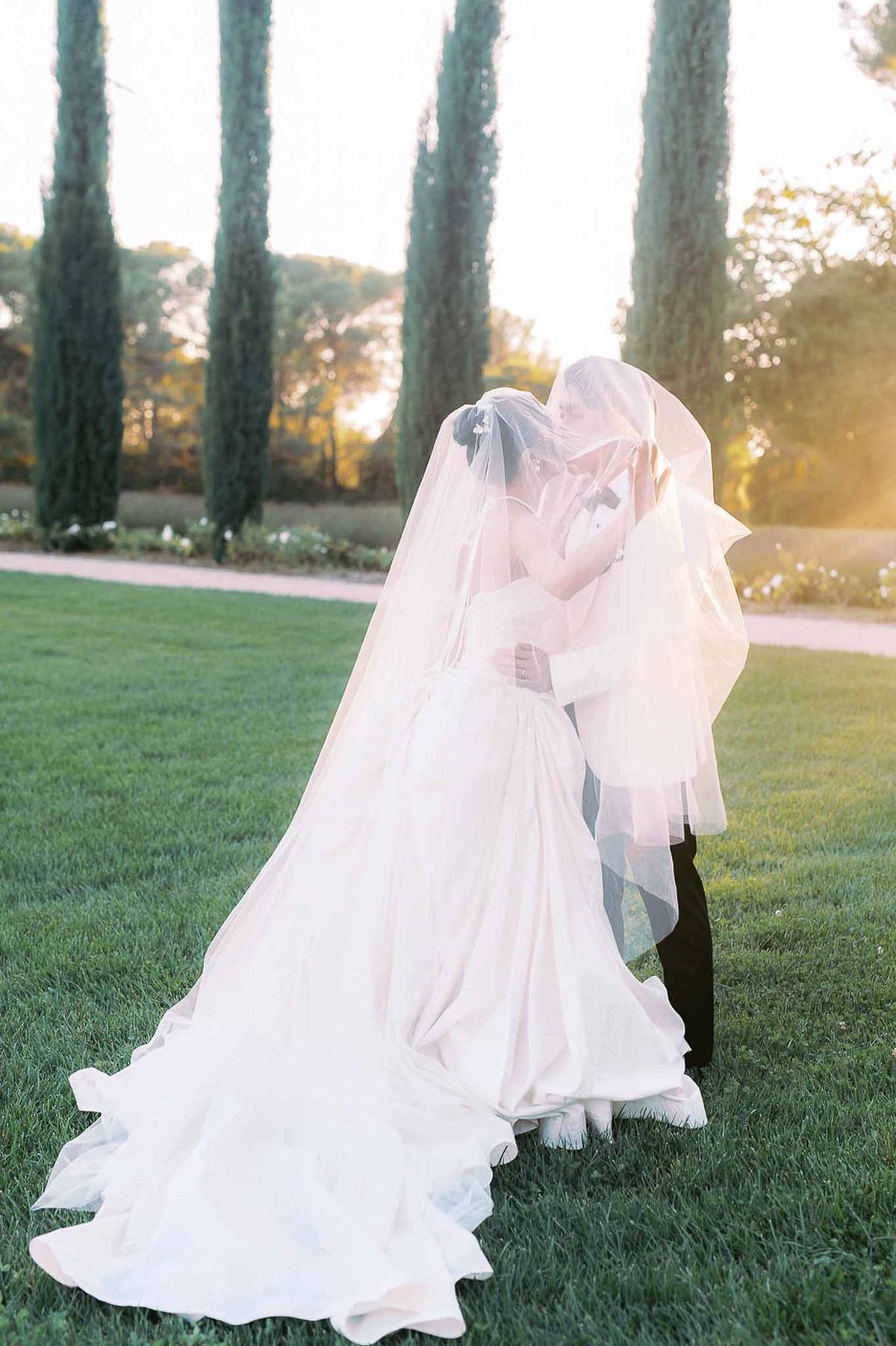 Couple wrapped in veil at sunset on cypress lawn at Château de la Gaude