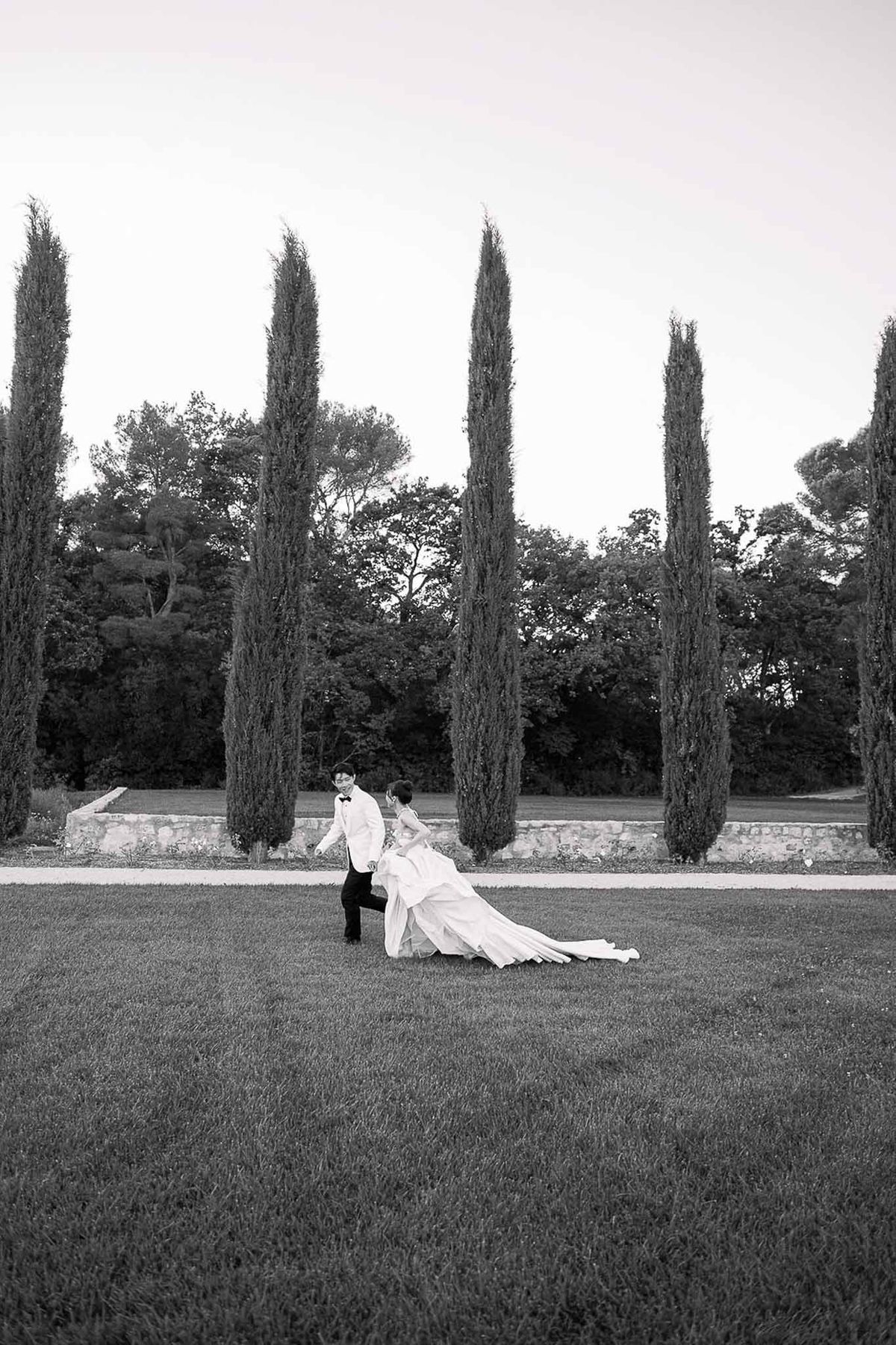 Groom dipping bride on lawn with cypress trees in black and white at Château de la Gaude