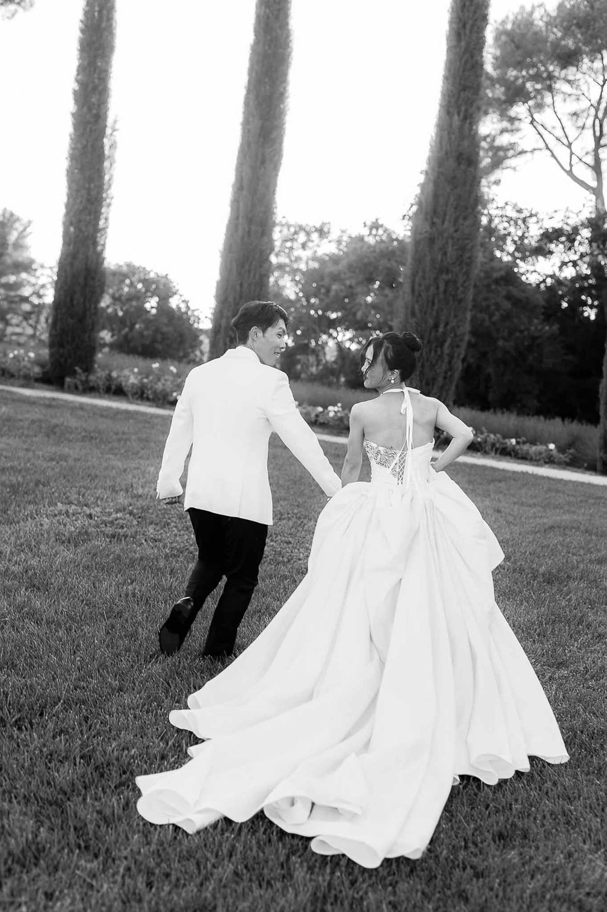 Couple running hand in hand across lawn at sunset in black and white at Château de la Gaude